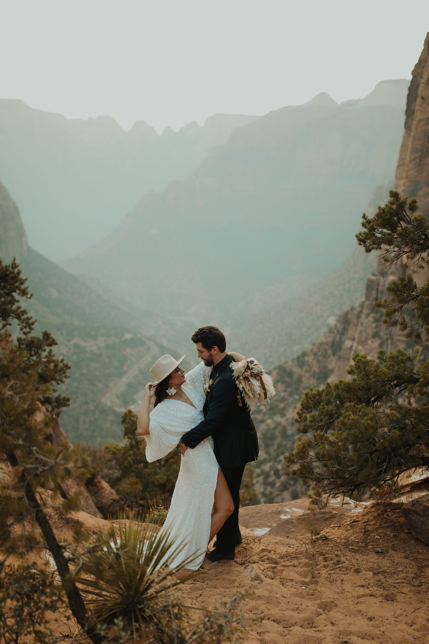 Couple in formal attire kissing with tan rocks behind them