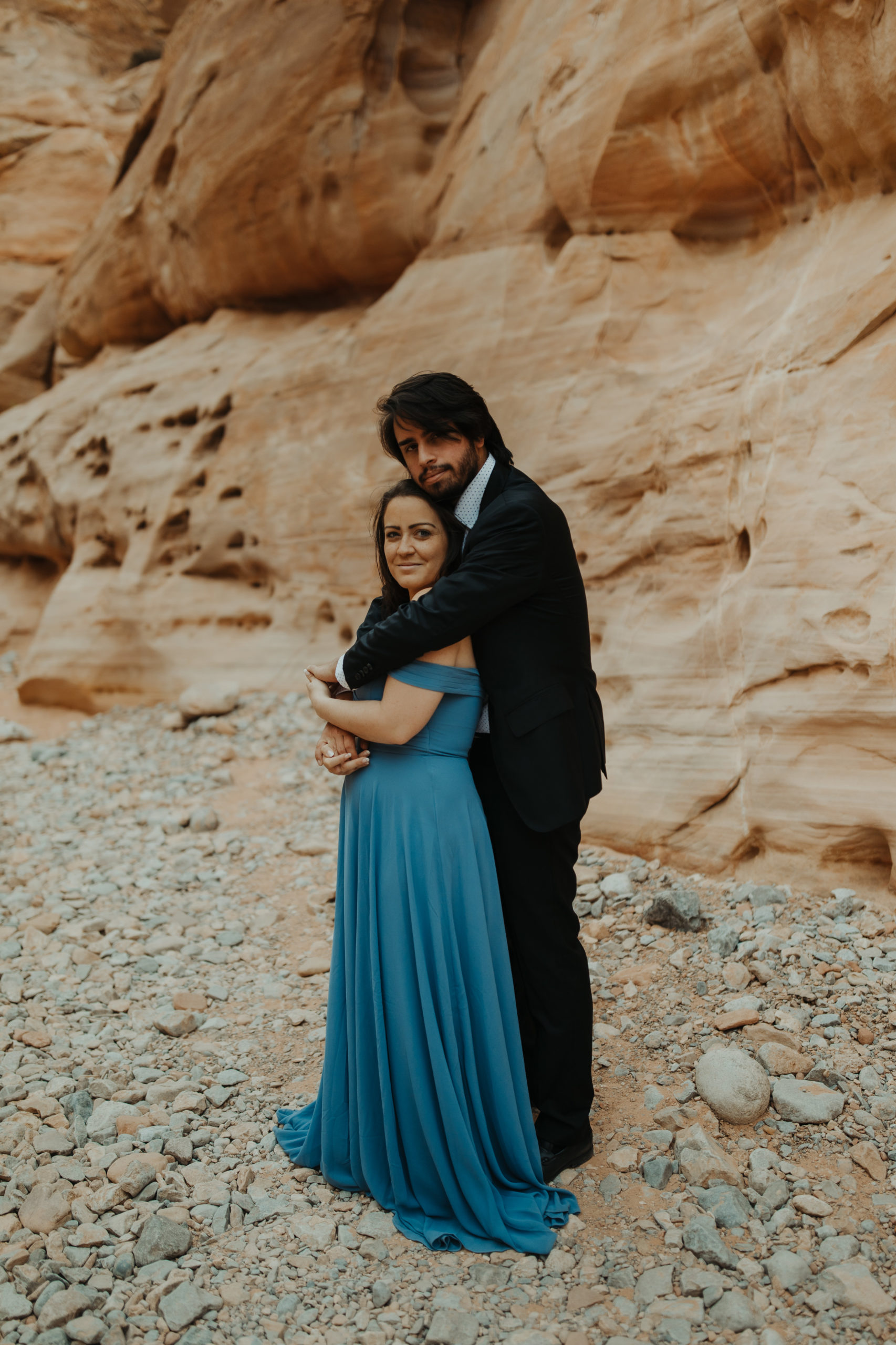Couple in formal attire standing next to each other with tan rocks behind them