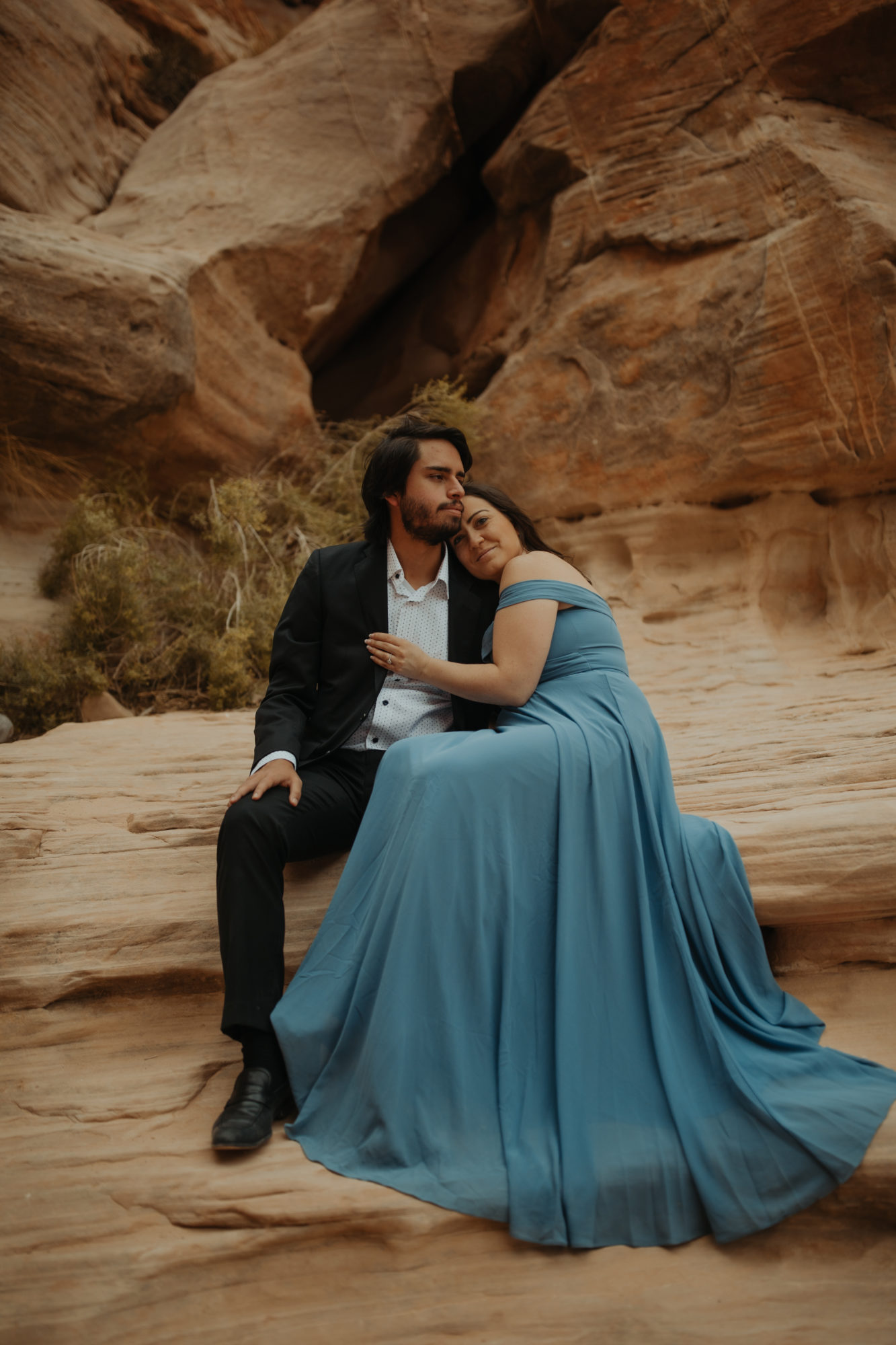 Couple in Formal Attire sitting on a tan large rock