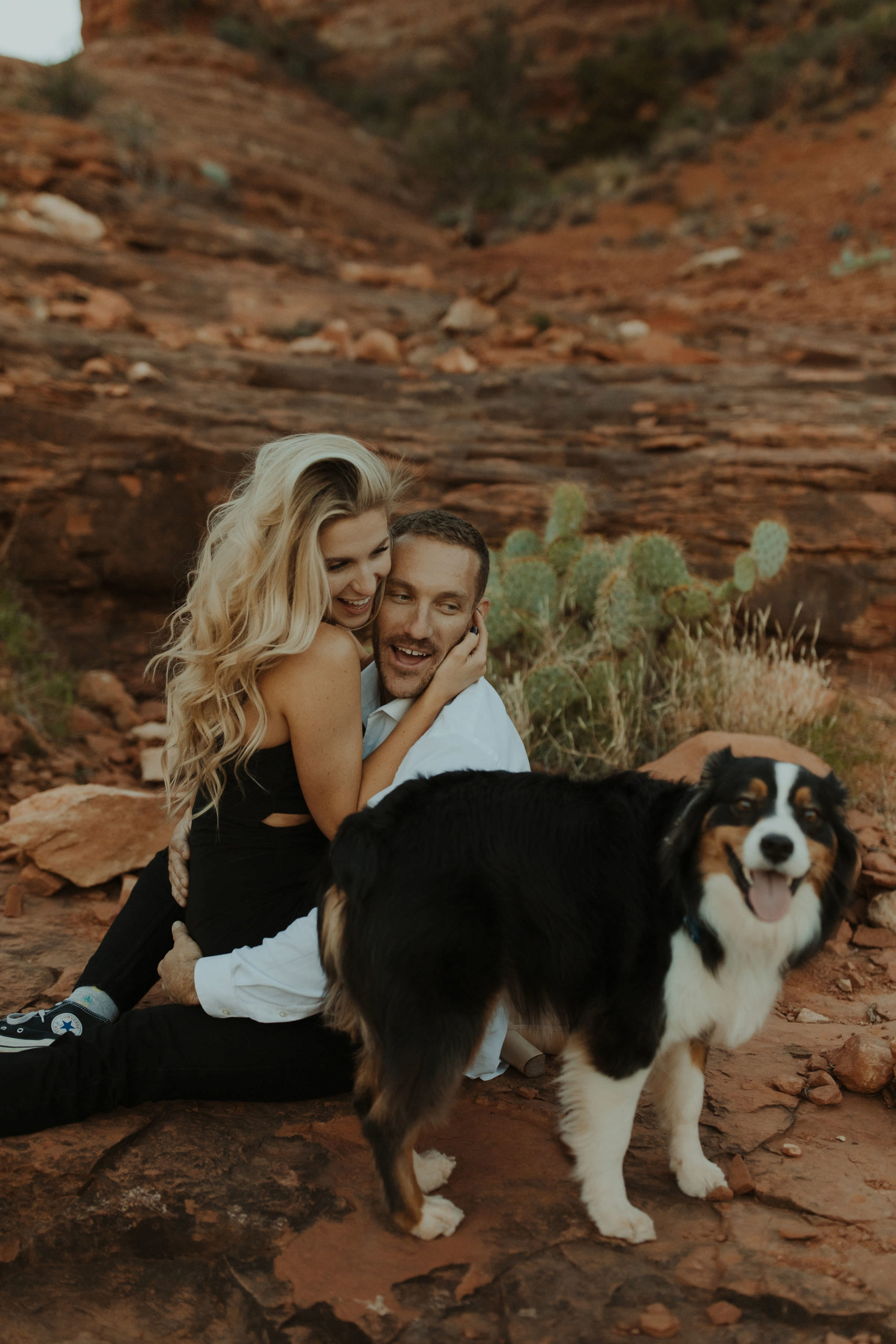 Engagement photos with couple and their dog cuddling in front of Cathedral Rock in Sedona