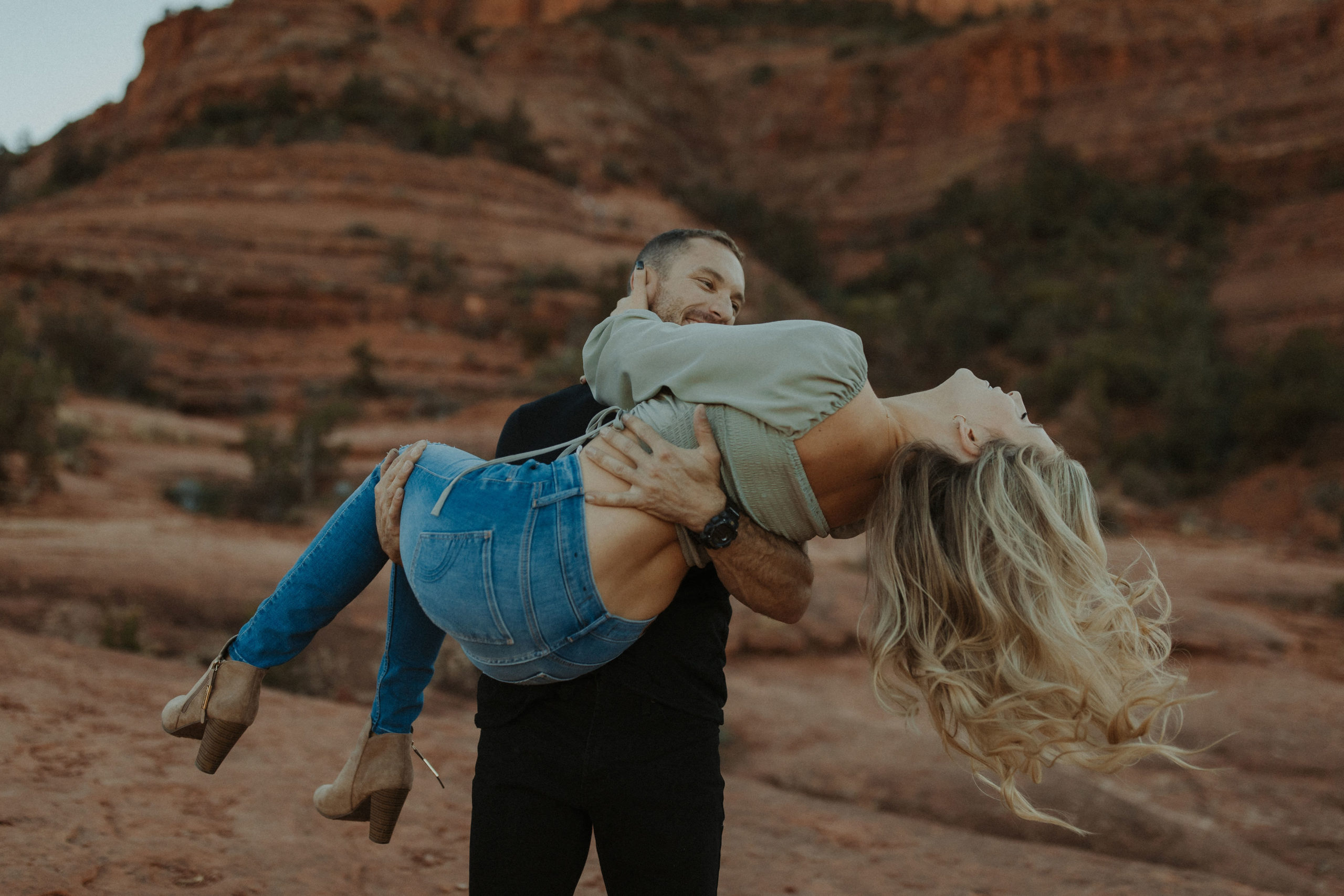 Fun couple engagement photos with man holding girl in his arms with Cathedral Rock in Sedona