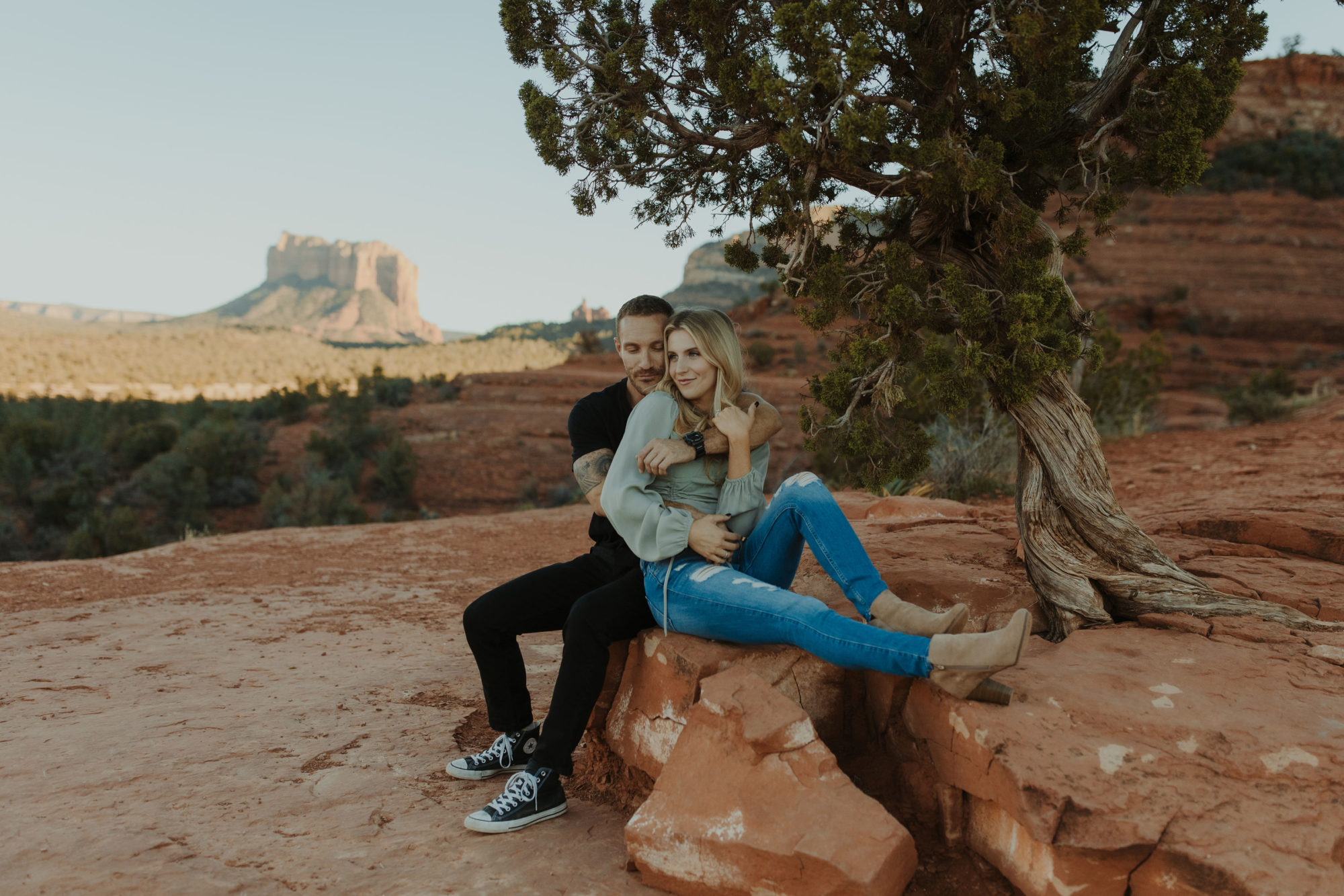 Engagement photos with couple cuddling in front of Cathedral Rock in Sedona next to a tree