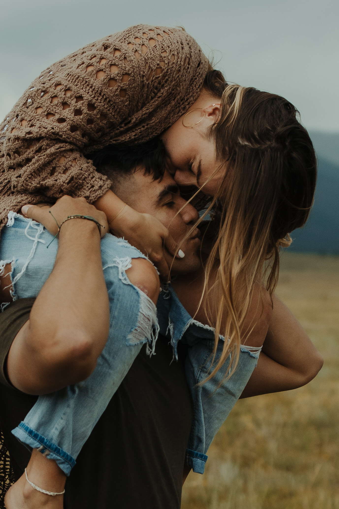 Grunge couple with girl on guys' shoulder kissing with Colorado mountains behind them