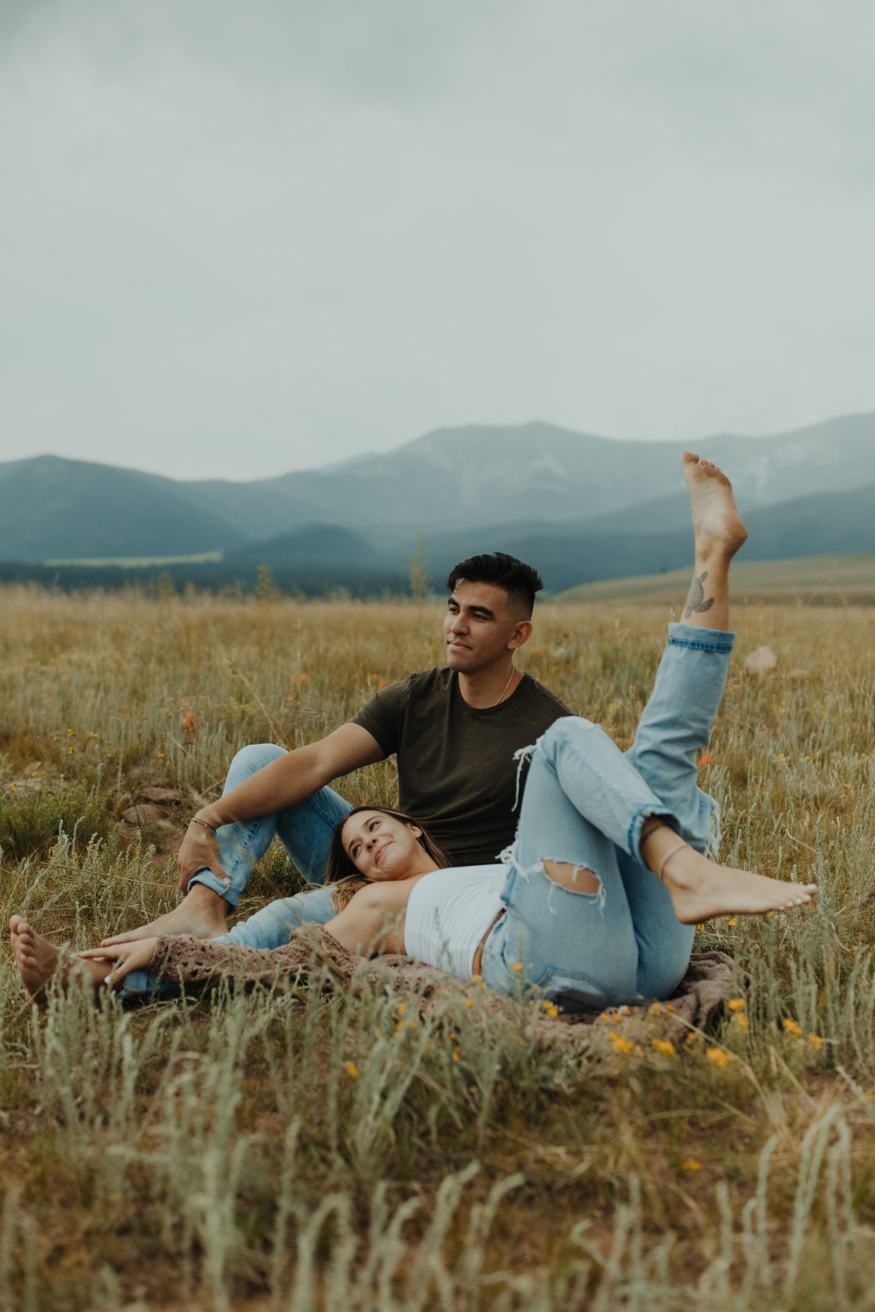Grunge couple laying in grass with Colorado mountains behind them
