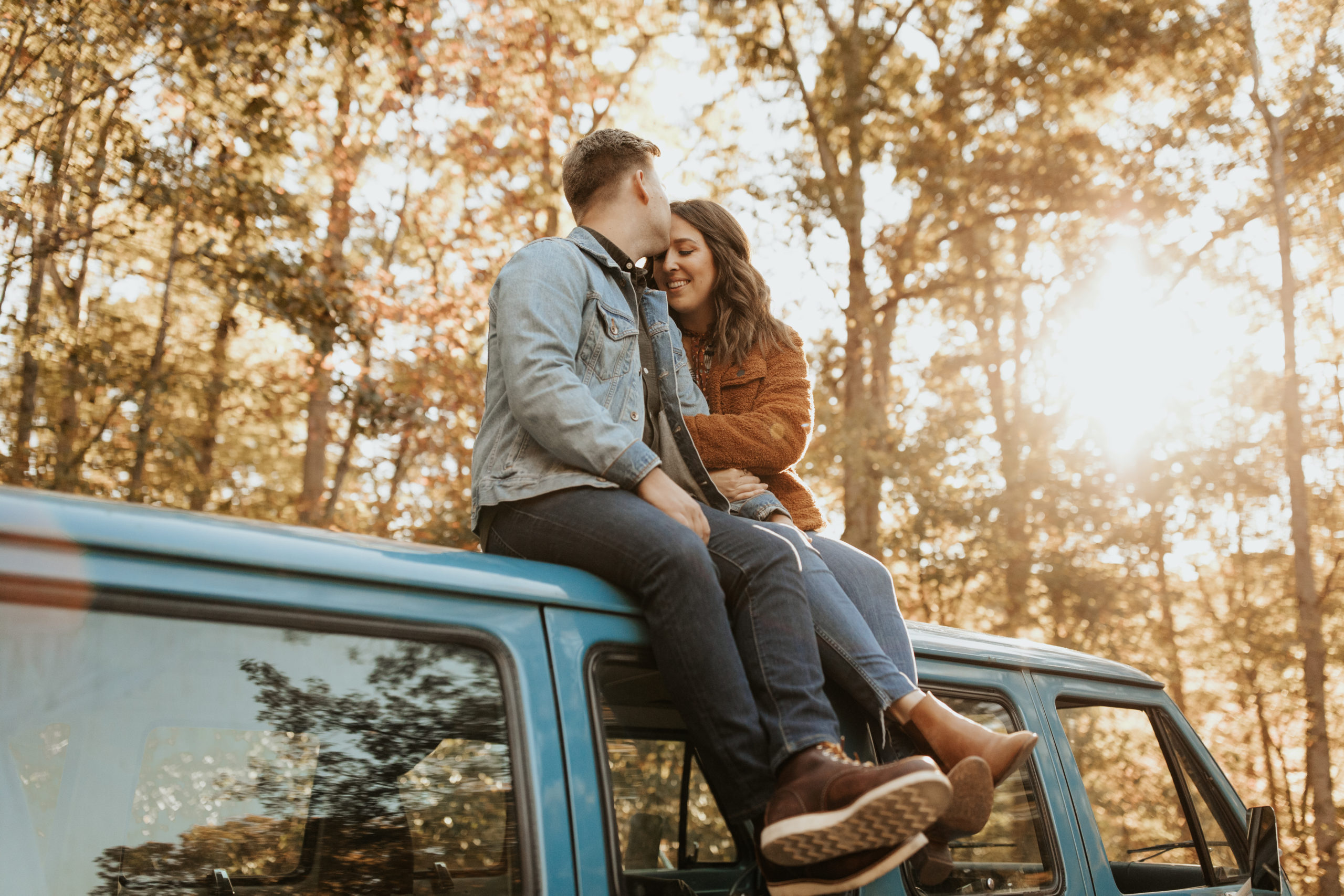 couple sitting on top of their campervan while boyfriend is kissing girlfriends forehead