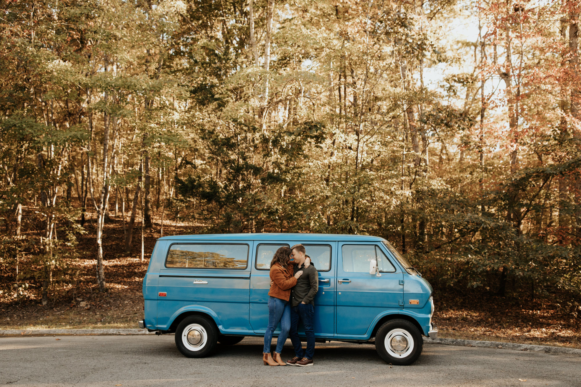 Cute couple standing in front of their blue camper van in the forest