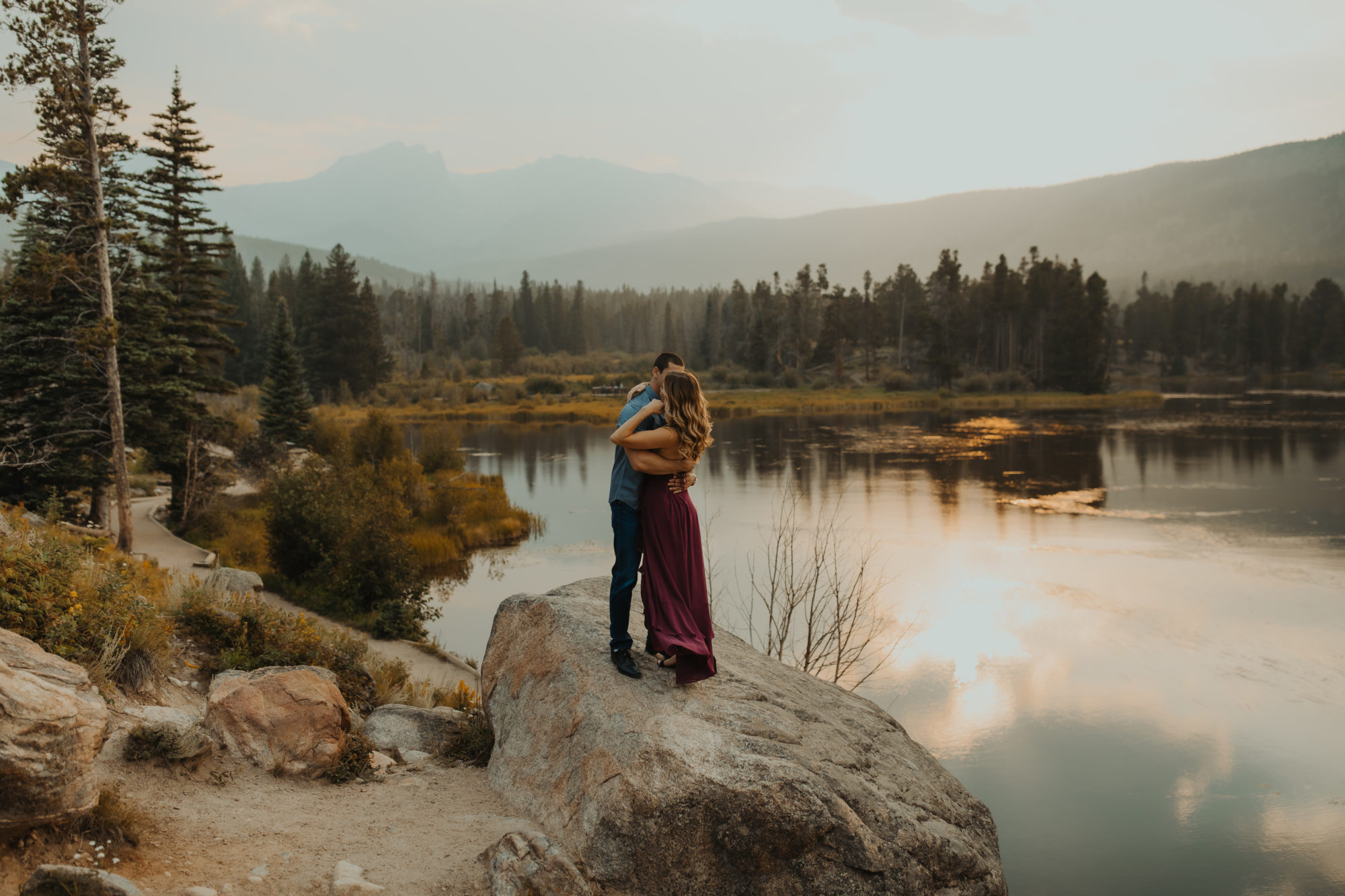 couple standing on a rock in front of the lake with the mountains in the background