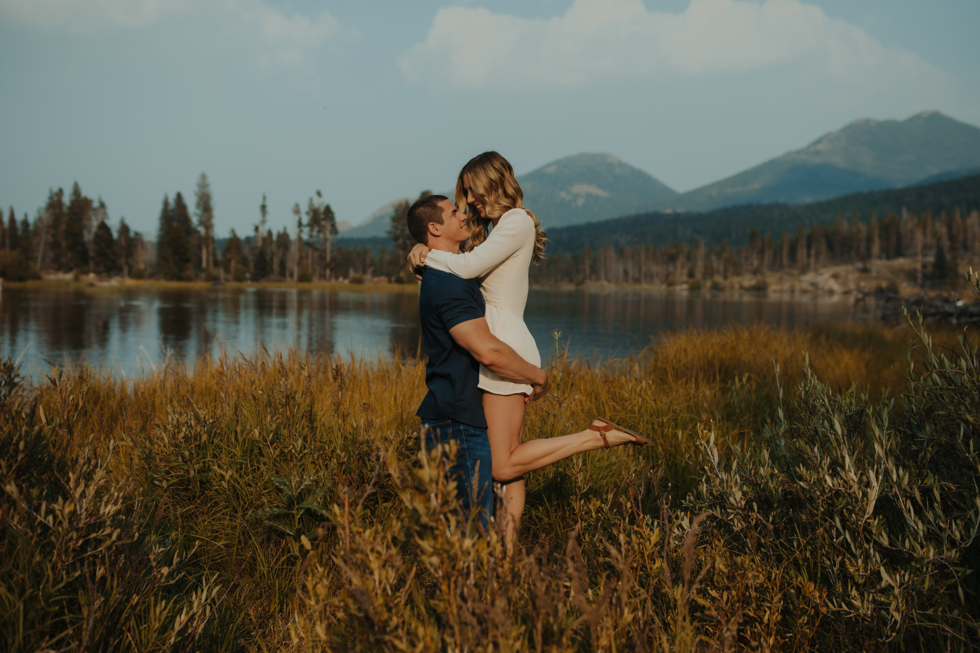 fiance picking his girlfriend up in a meadow in the PNW with the mountains in the background