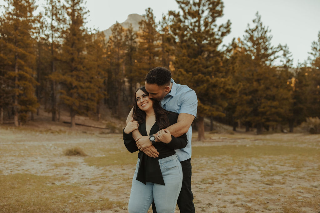 boyfriend standing behind his girlfriend kissing her on the cheek in a field in mt. charleston nevada