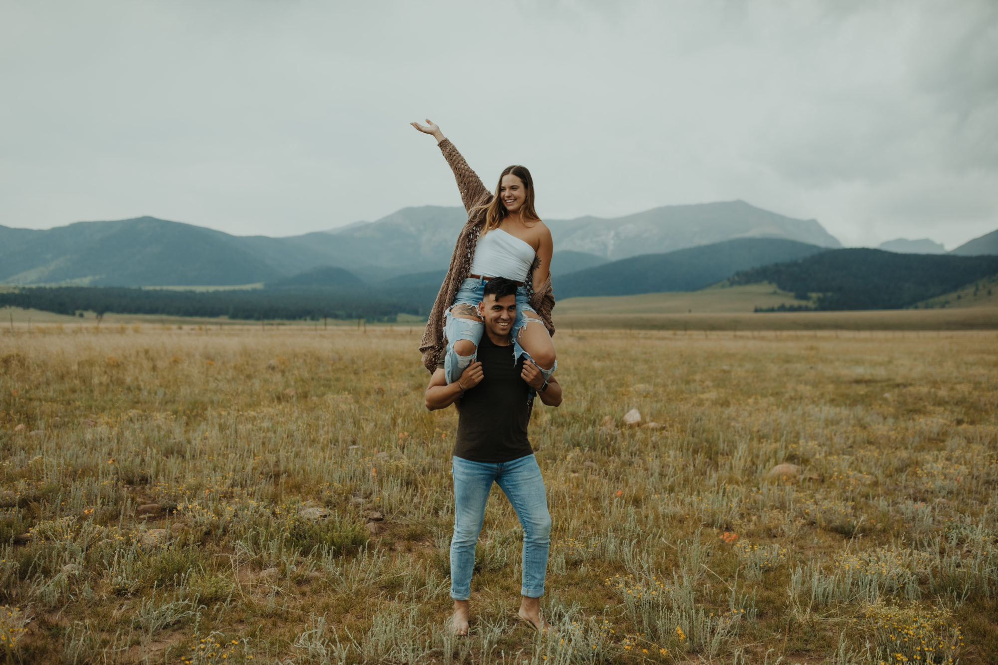 boyfriend giving his girlfriend a shoulder ride in a field in the mountains