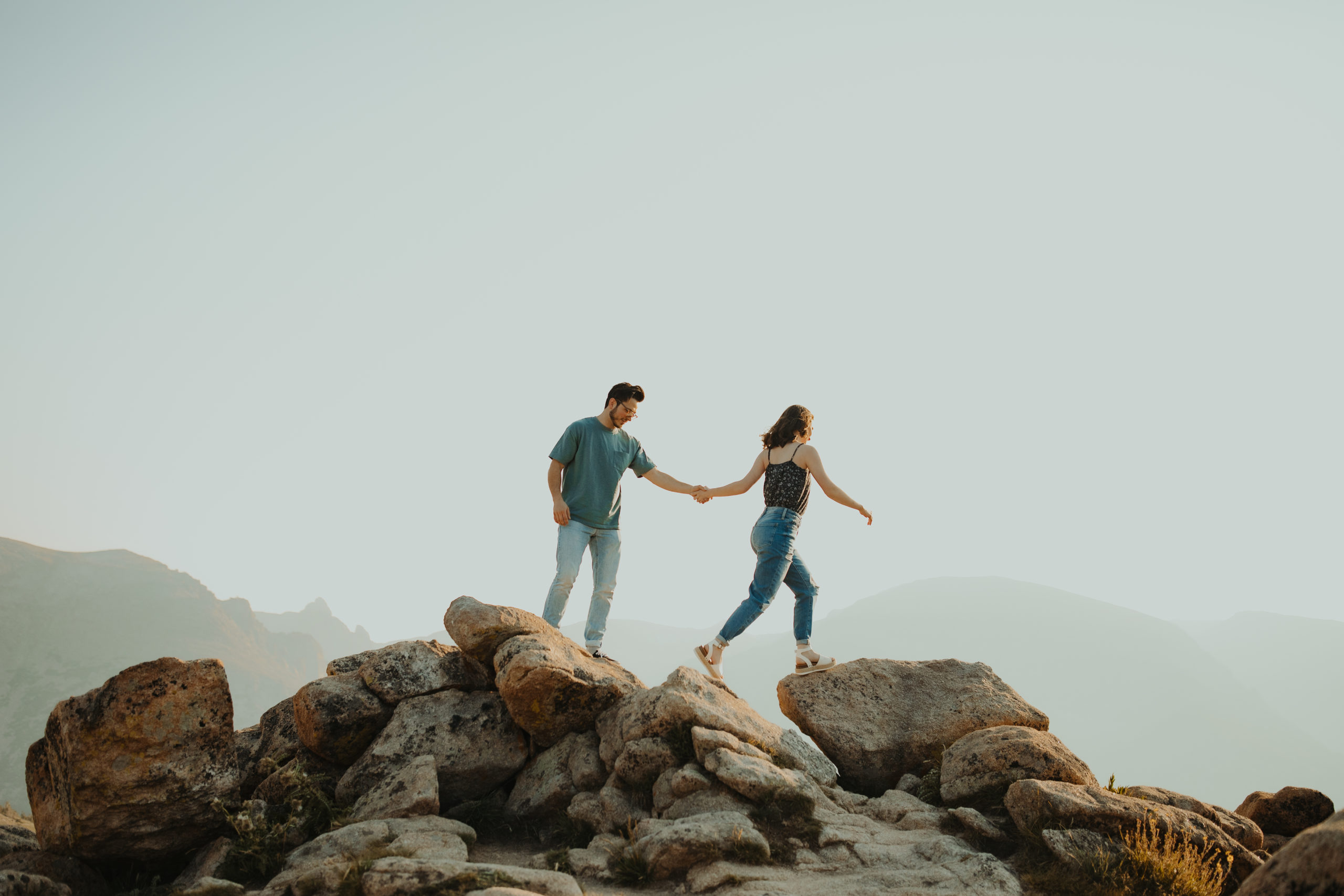 Couple jumping across rocks while holding hands