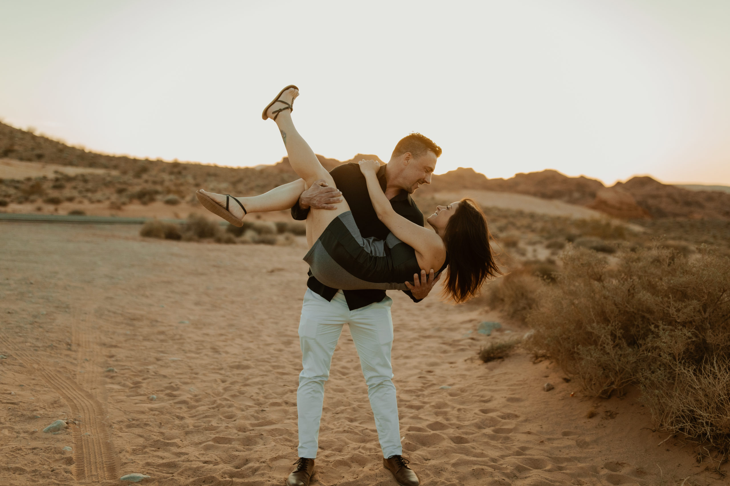boyfriend picking his girlfriend up and dipping her backwards during their engagement session in the desert