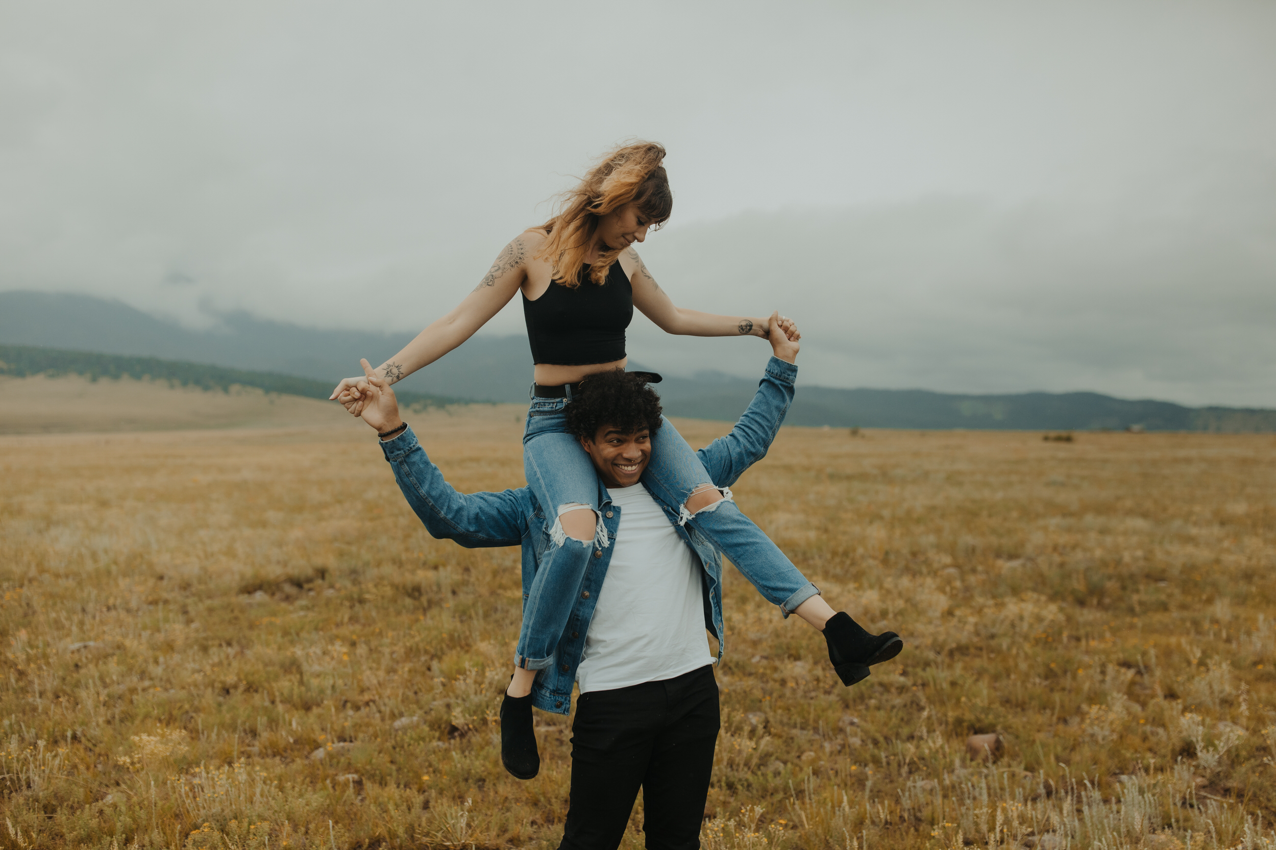 alt couple with boyfriend giving girlfriend piggy back ride in the mountains