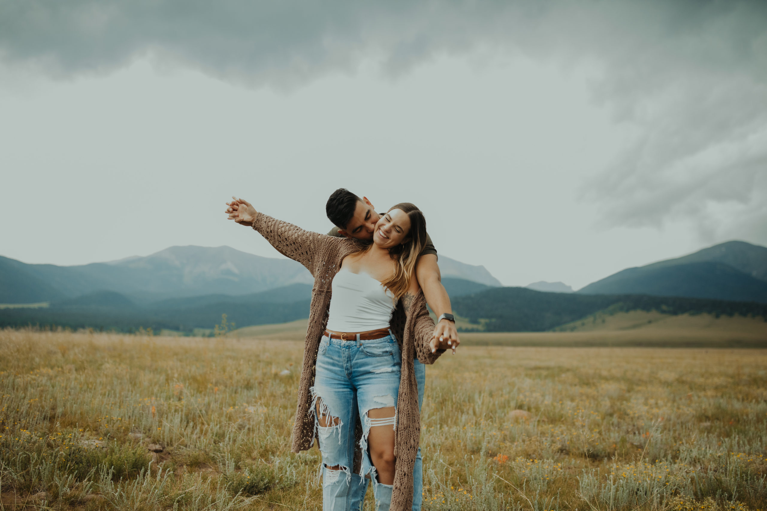 boyfriend kissing girl on the neck as they do playful airplane arms during couples photoshoot in the mountains