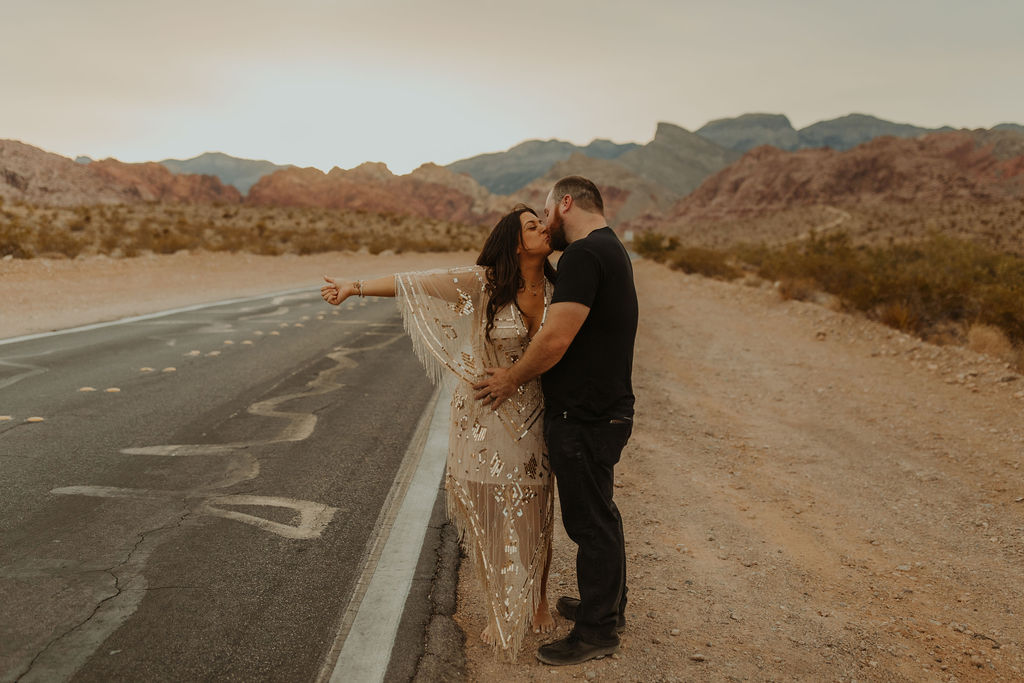 husband aand wife jokingly hitch-hiking in the desert during their vow renewal photoshoot