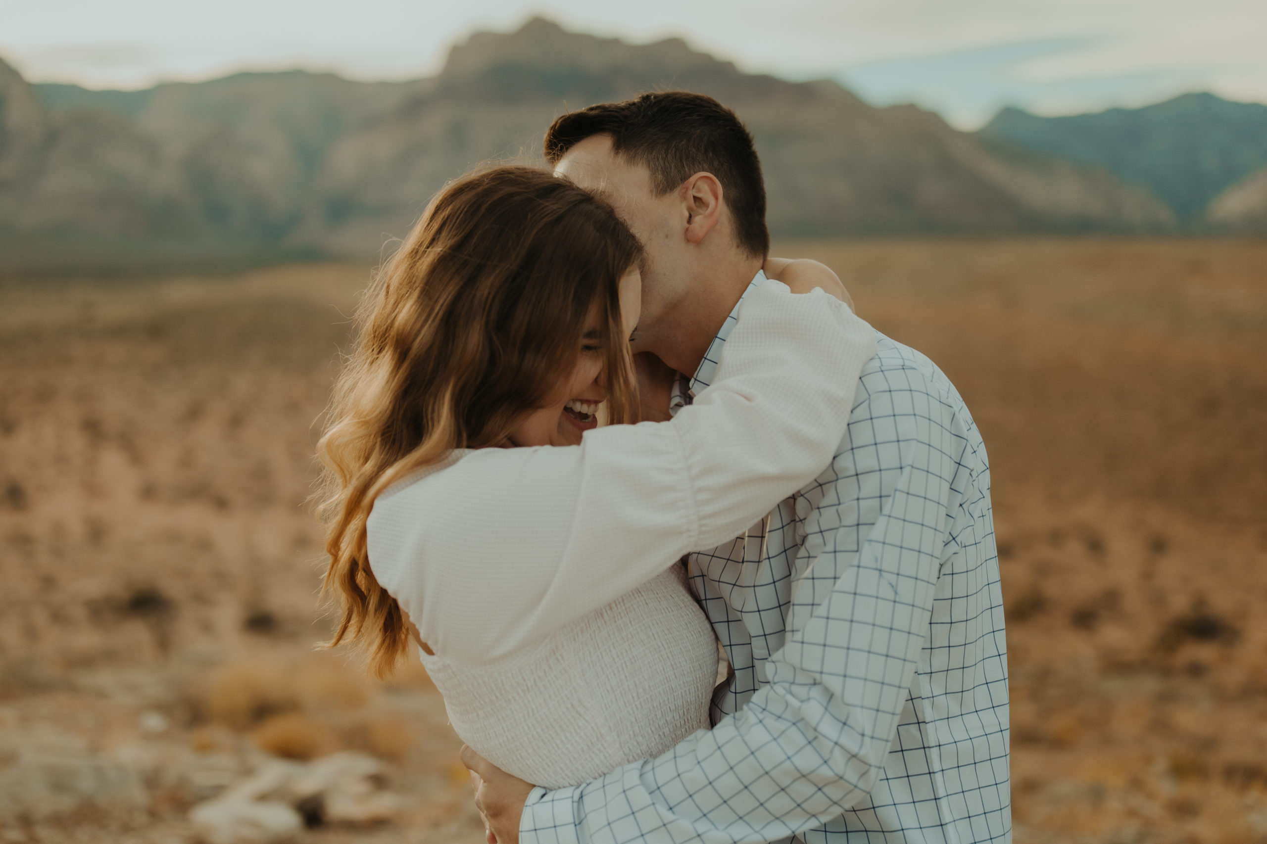 boyfriend whispering something into girlfriends ear during engagement session in the desert