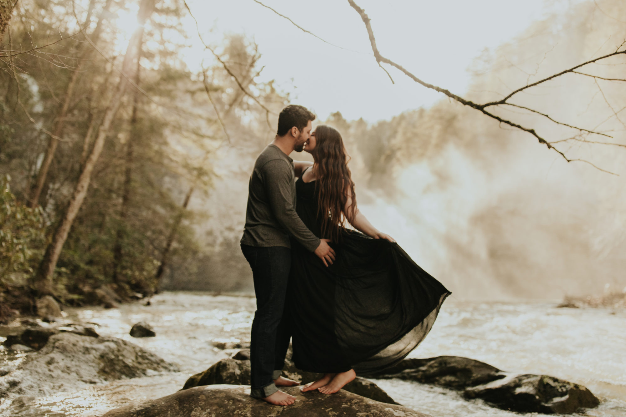 couple kissing in front of waterfall while girl plays with her dress