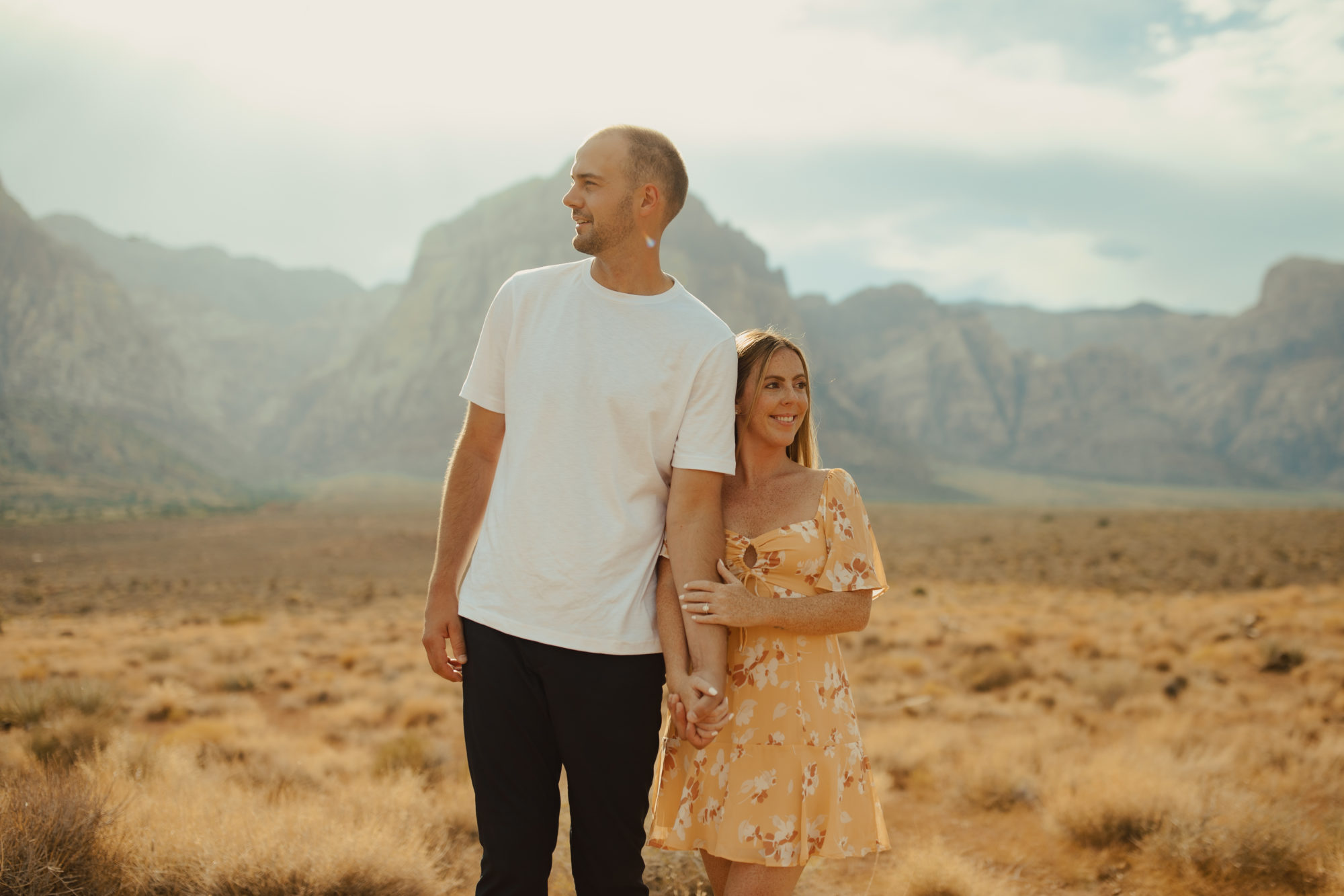 couple standing shoulder to shoulder holding hands and looking in different directions while standing in the desert