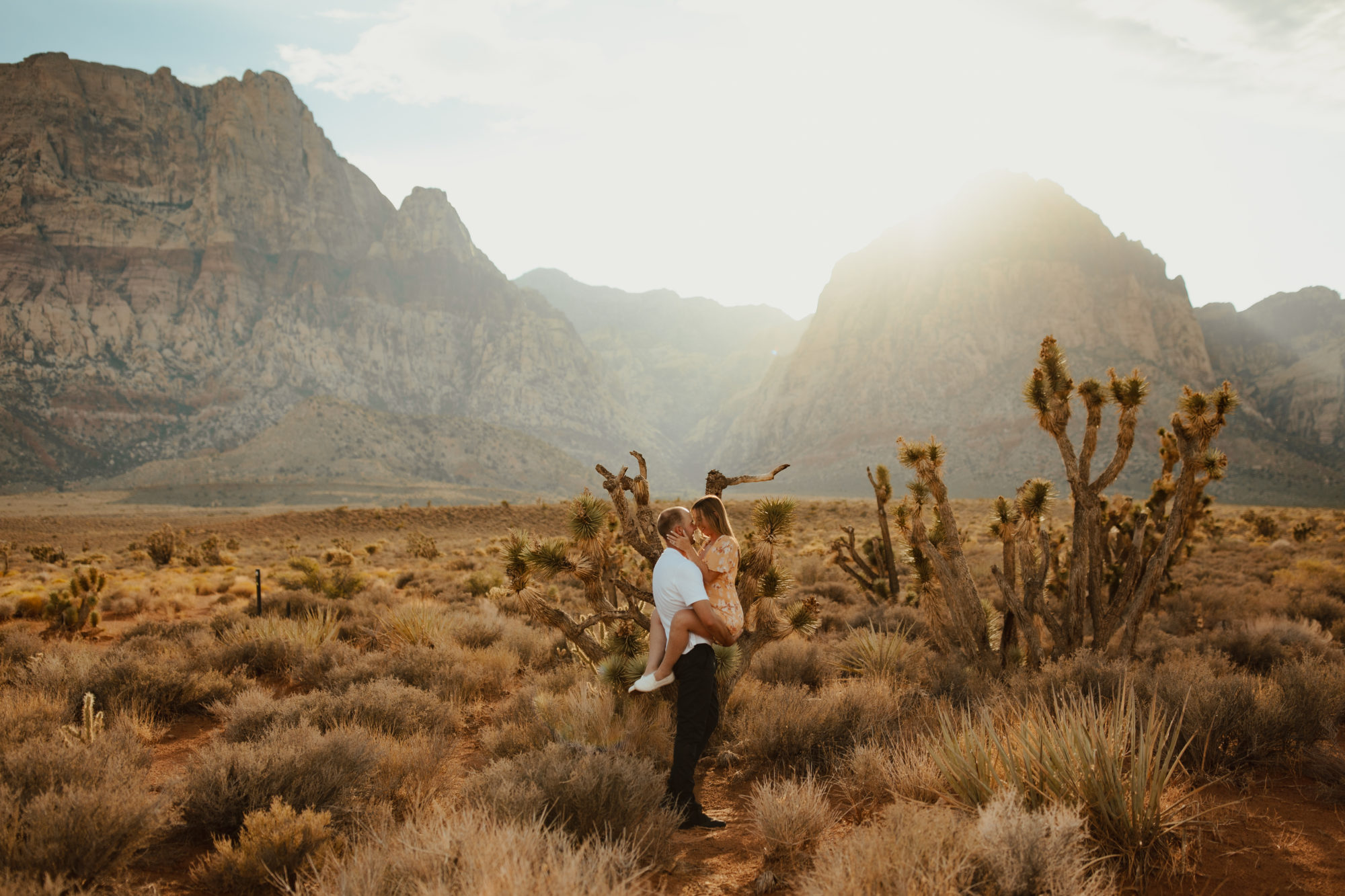 fiance picking his girlfriend up and kissing her during golden hour in the desert 