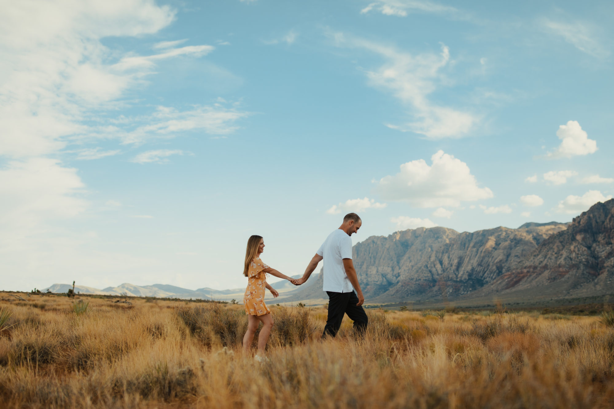 engaged couple walking through the field in the desert with mountains in the background