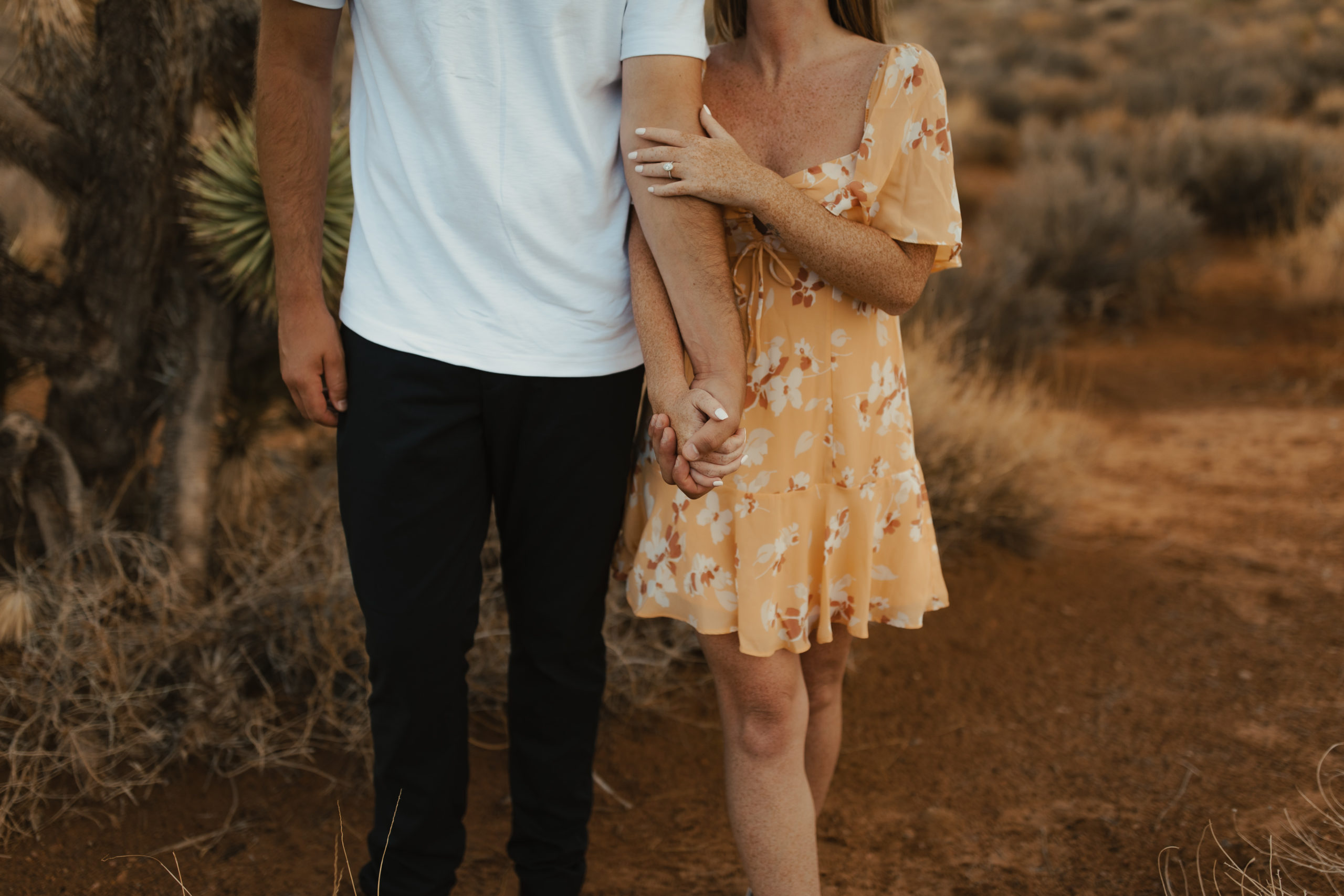 photo of engaged couple holding hands walking through the desert
