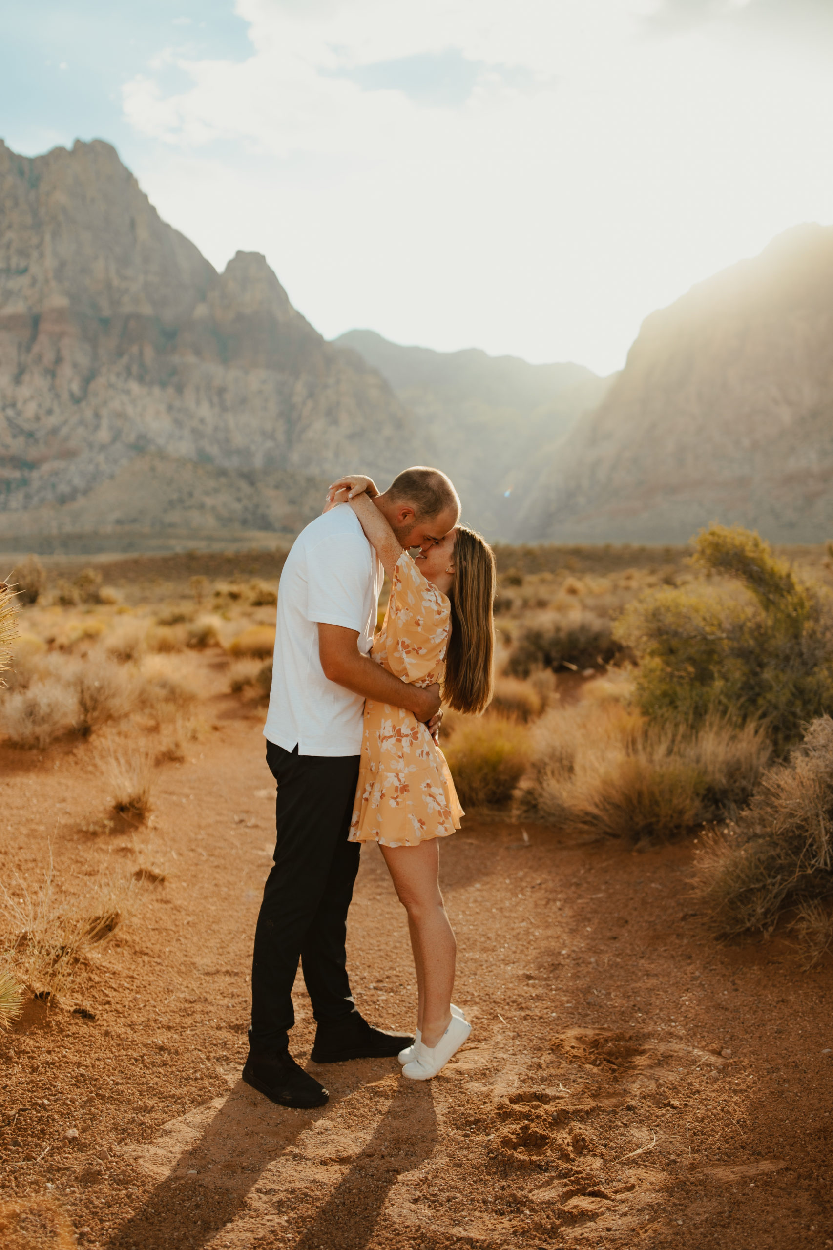 girlfriend standing on her tippy toes kissing her fiancé in the desert