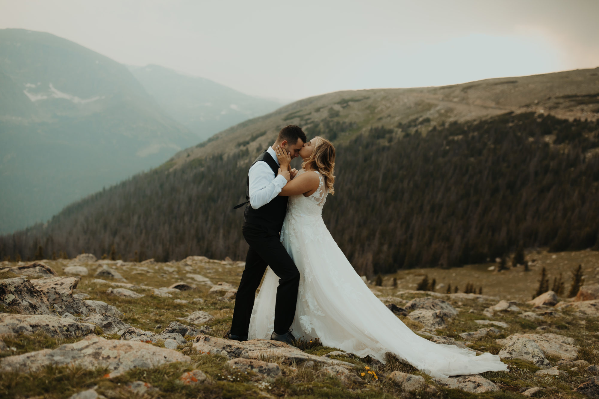 bride and groom standing on a mountain in rocky mountain national park while bride kisses the groom on the forhead