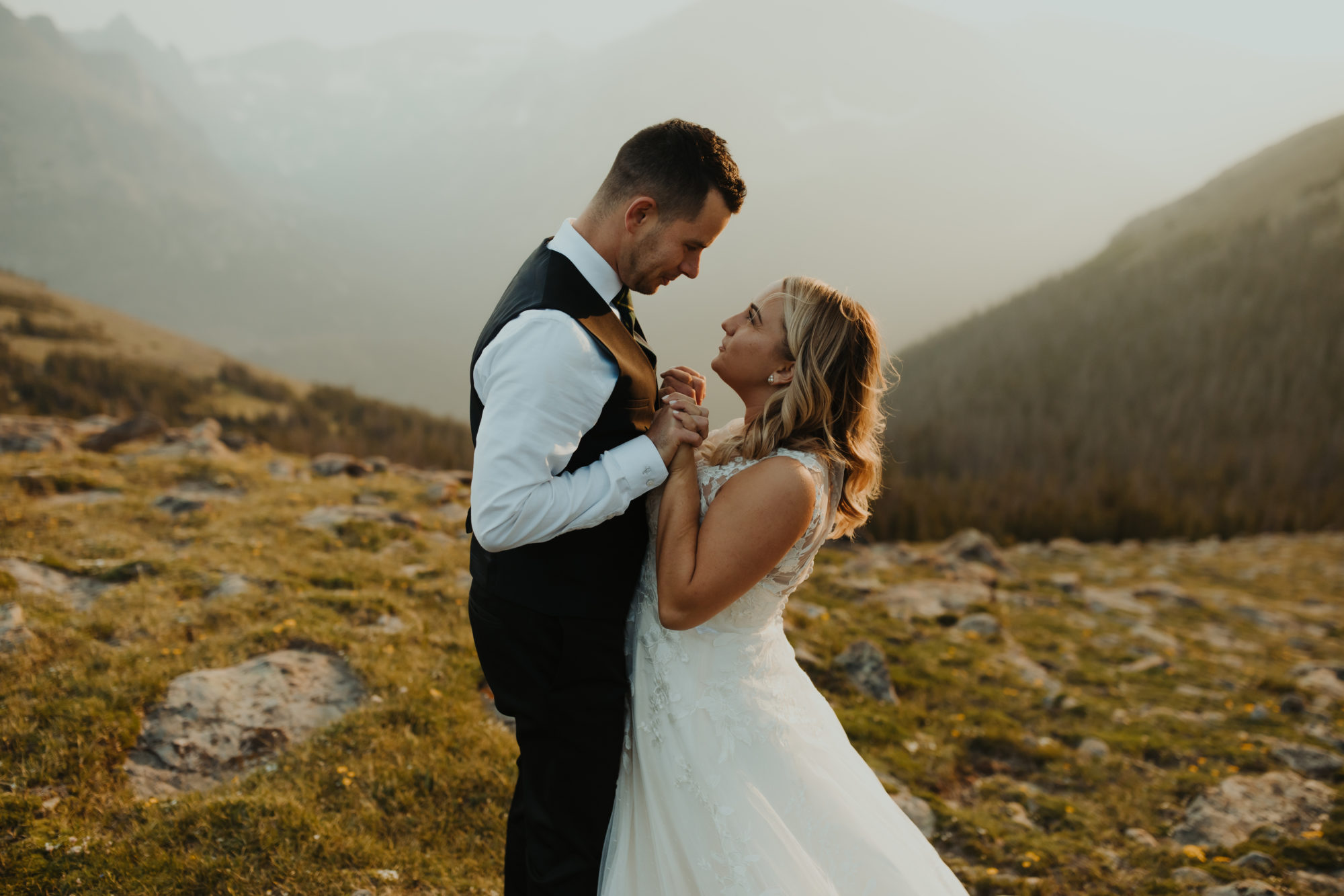 bride and groom facing each other while hands are interlaced in front of them while smiling at each other in rocky mountain national park