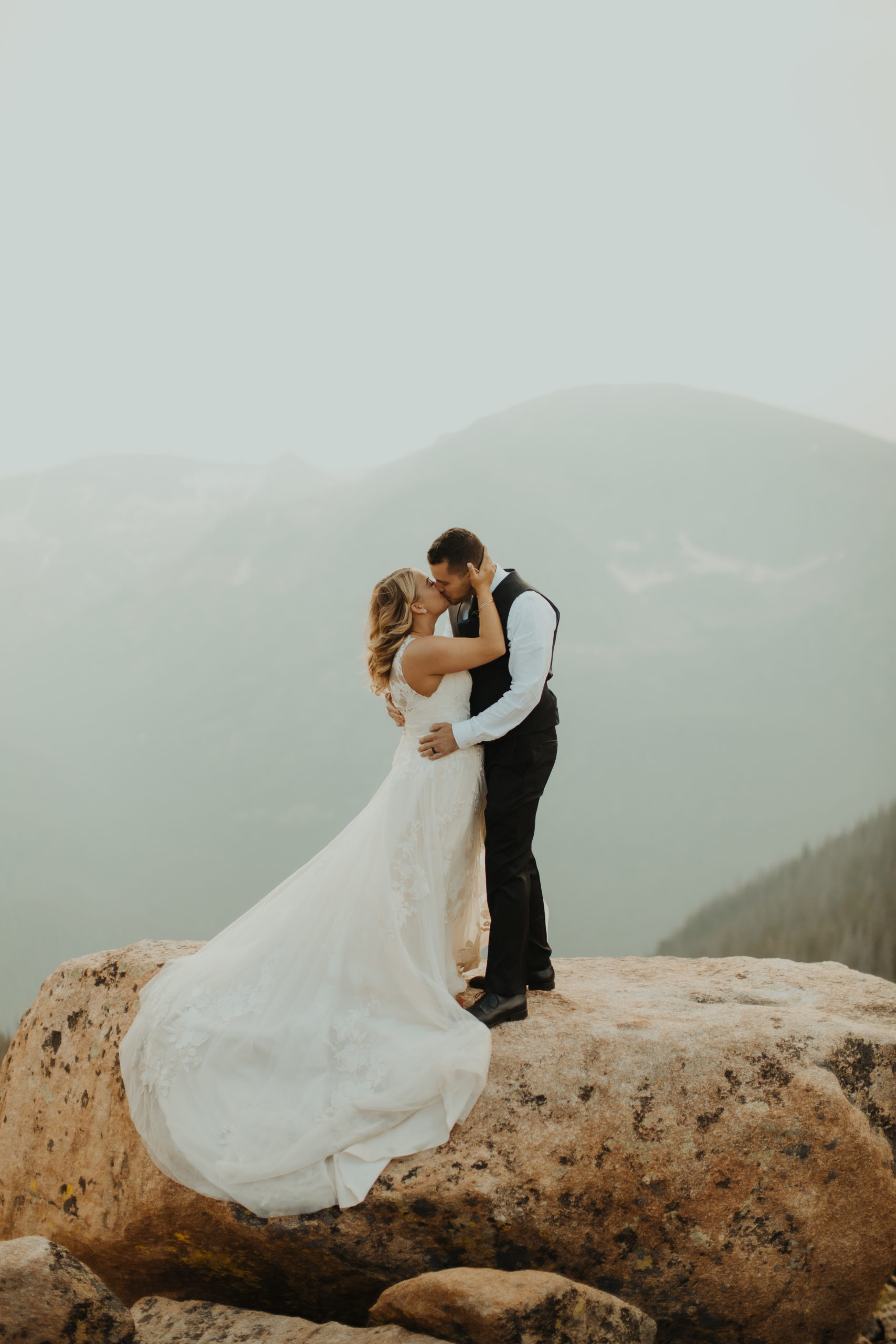 bride and groom standing on a rock in rocky mountain national park while kissing
