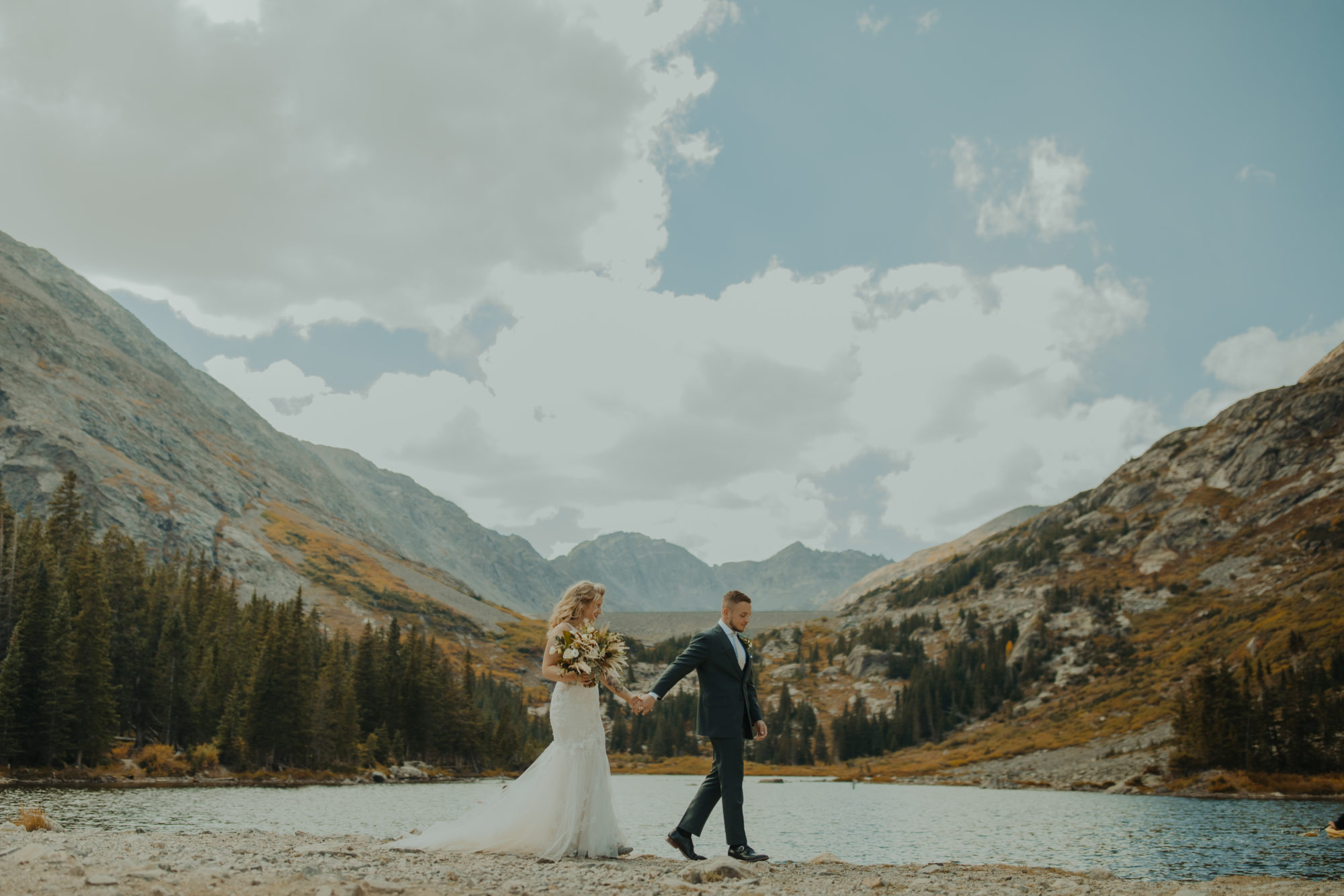 Couple walking along lake shoreline in wedding attire at blue lakes in breckenridge colorado 