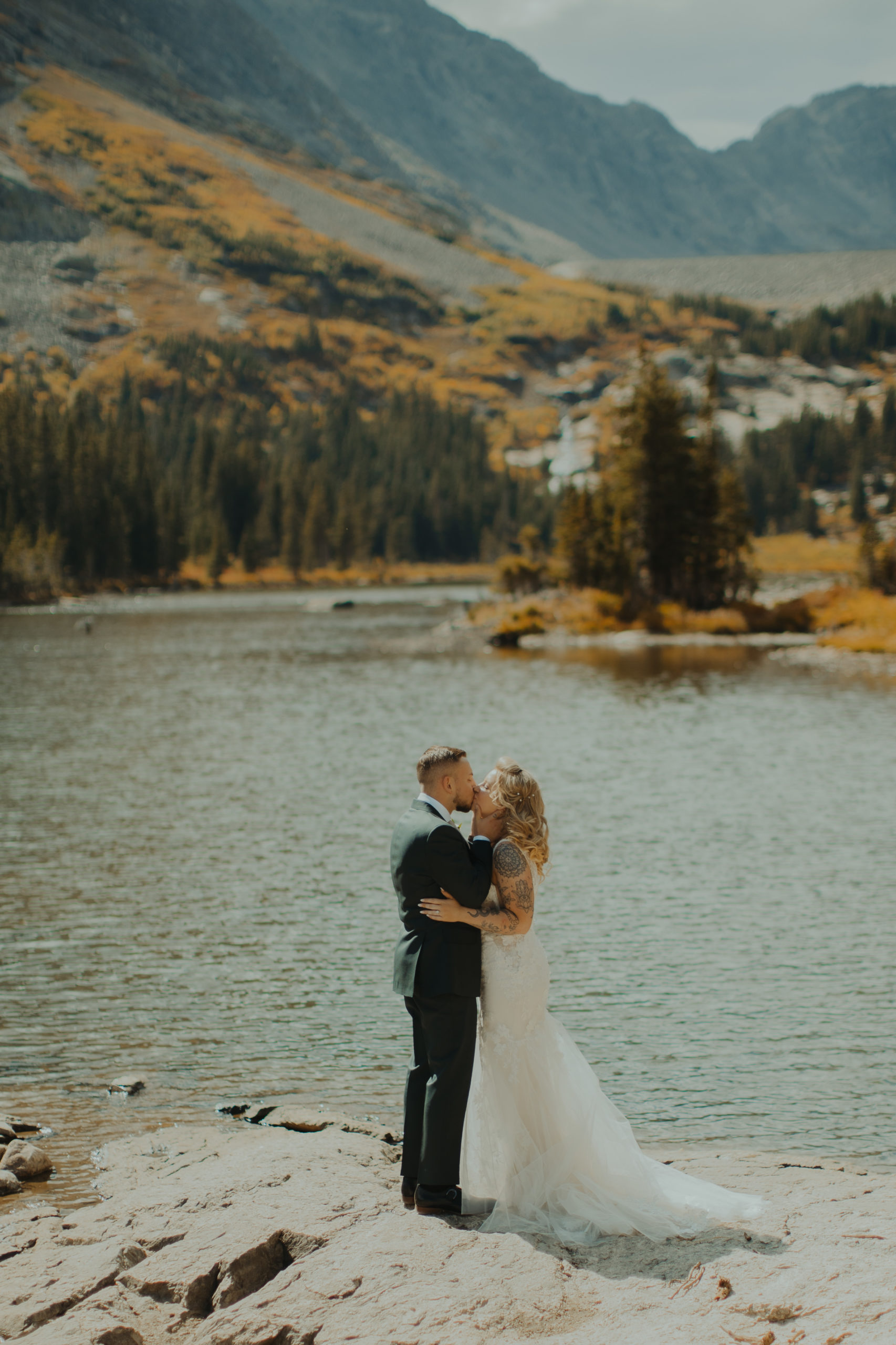 bride and groom kissing on the shore of a lake in breckenridge colorado