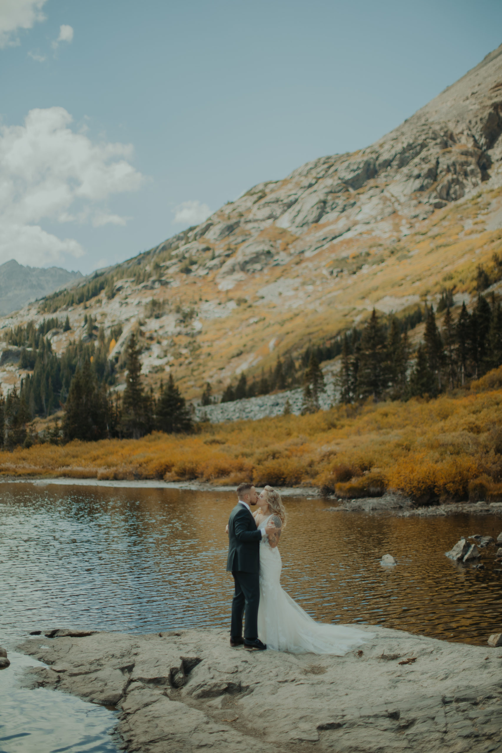 bride and groom kissing on a rock in a lake in colorado