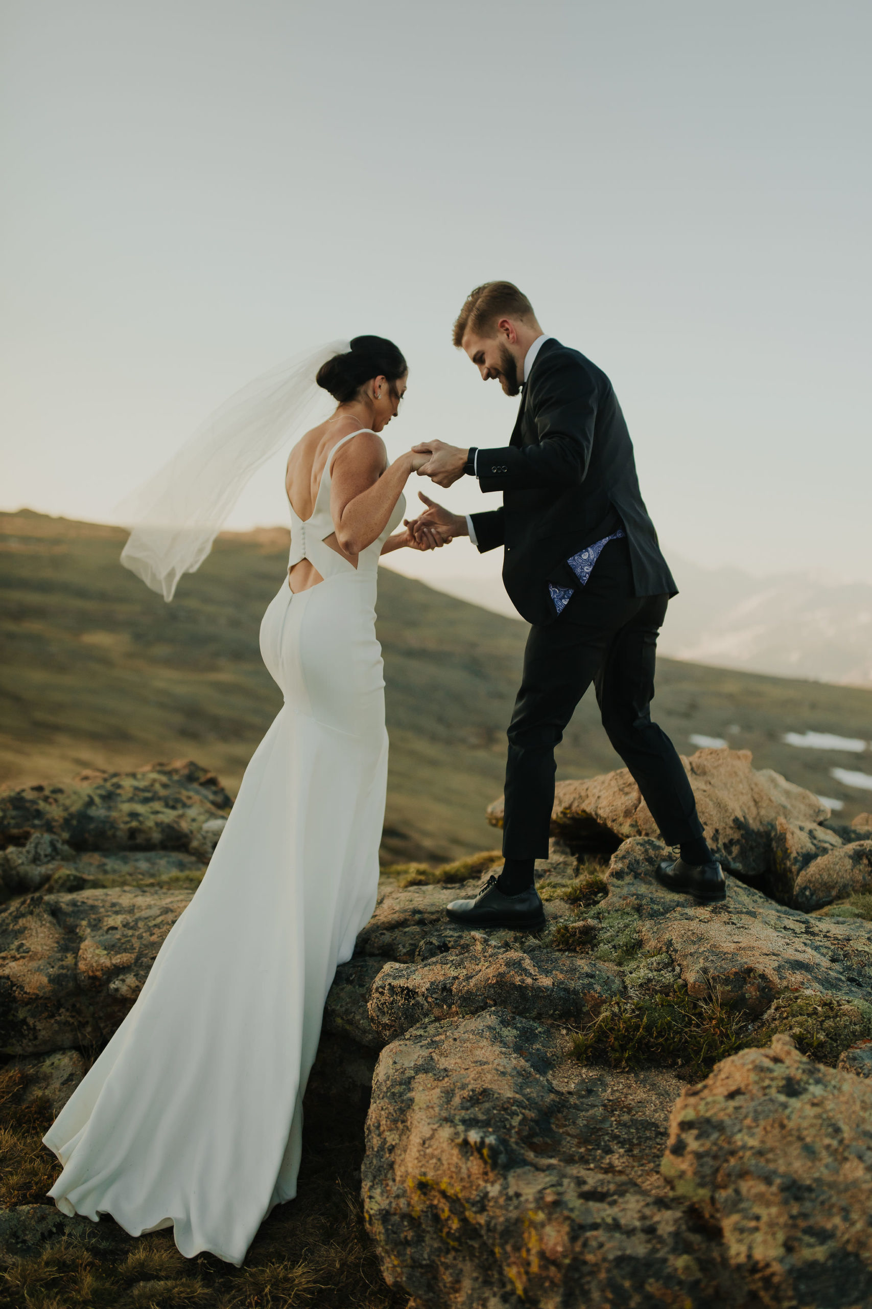 groom helping his bride up a rock in rocky mountain national park