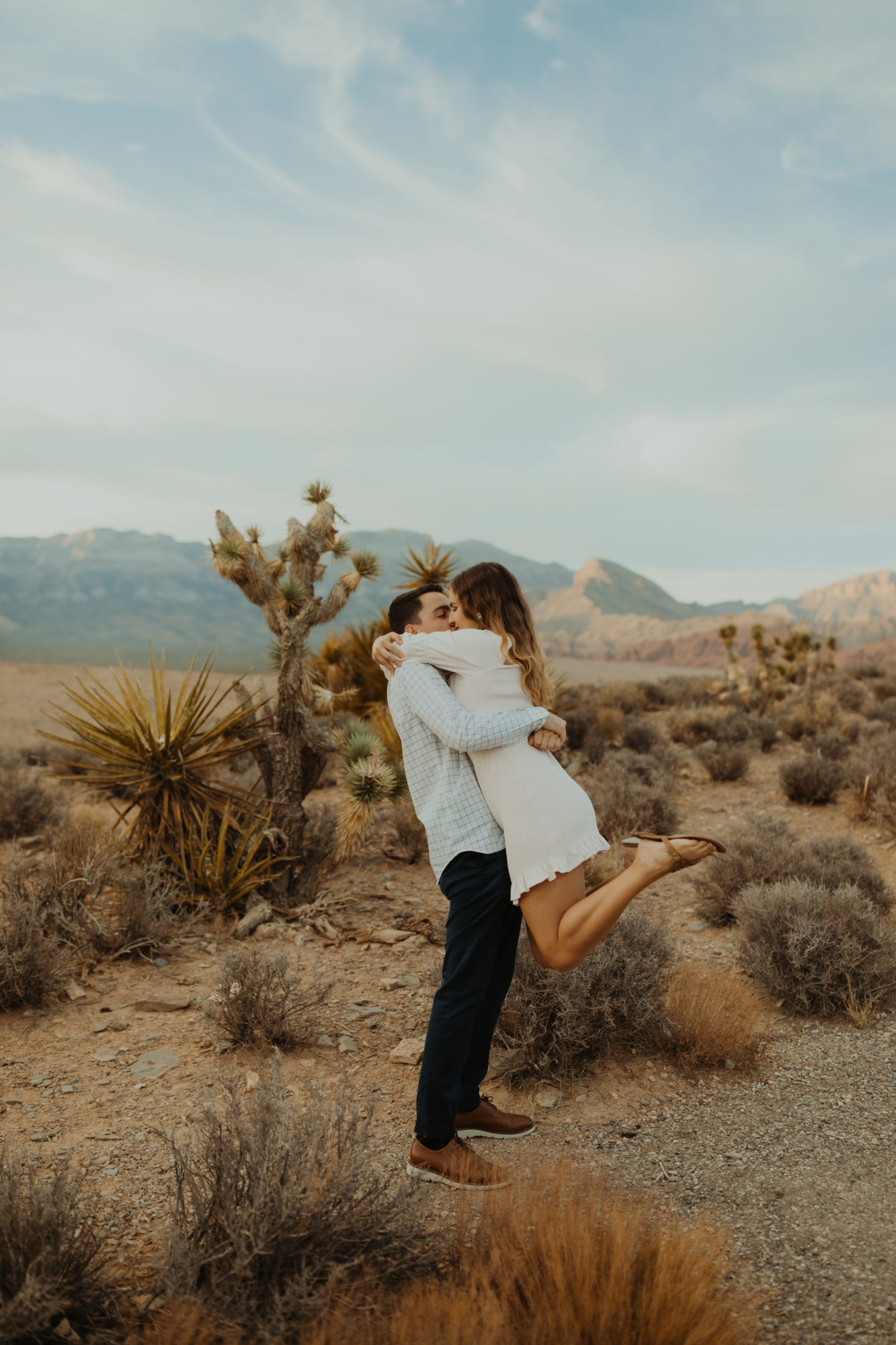 fiance picking up his girlfriend and kissing her after proposing to her in the desert