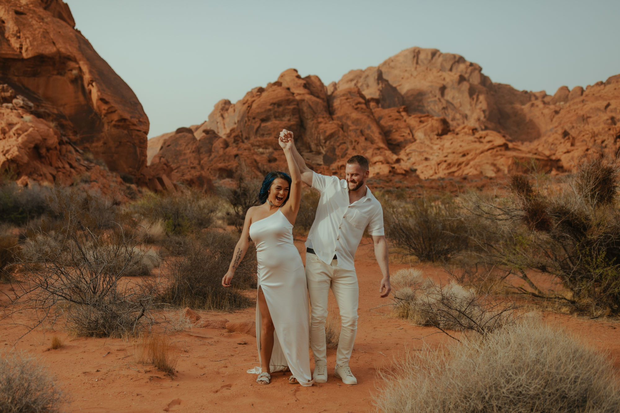 engaged couple walking and bumping their hips together as they walk through the desert during a dust storm