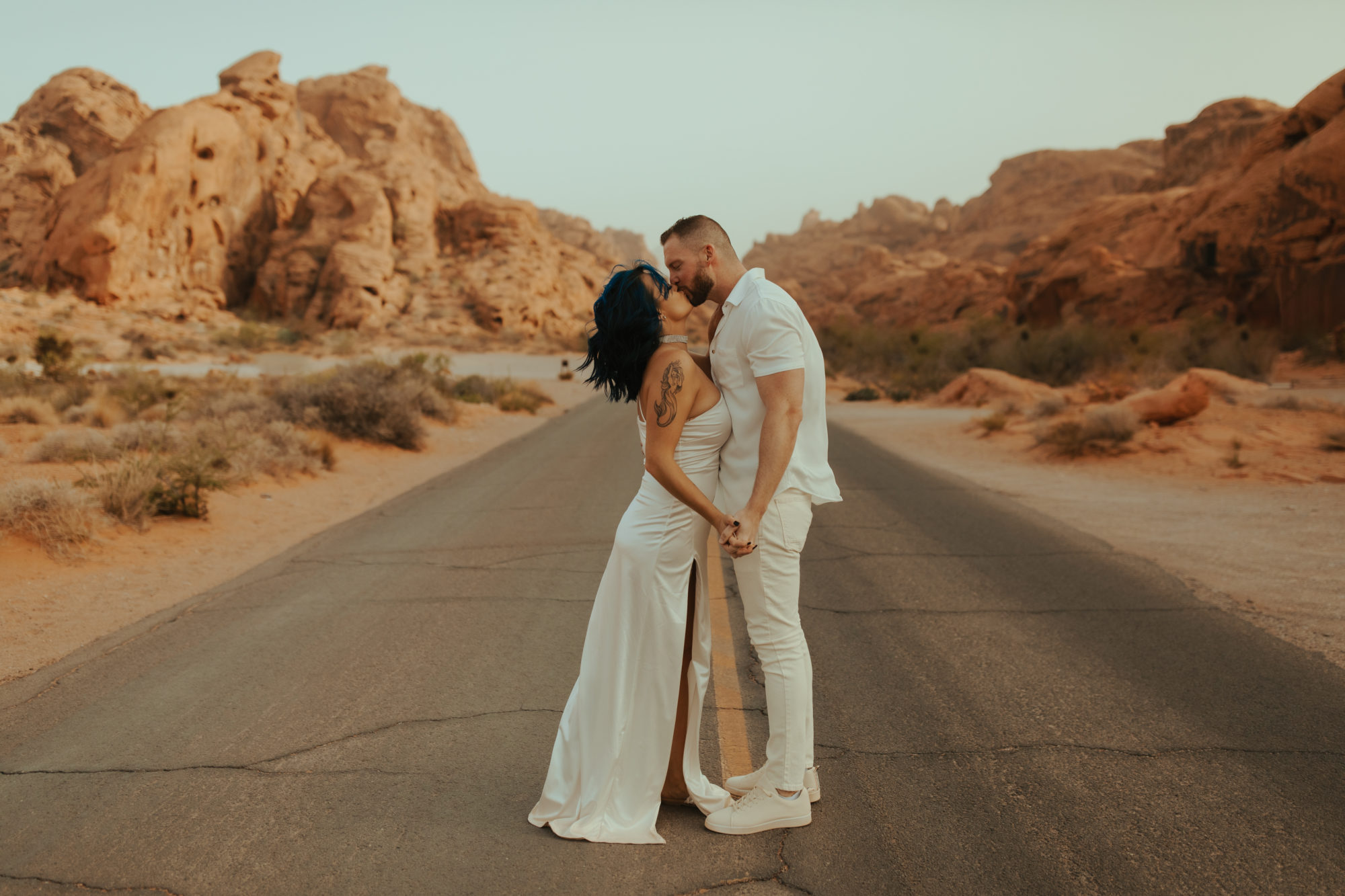 engaged couple standing in the middle of the road holding hands and kissing during a dust storm in valley of fire