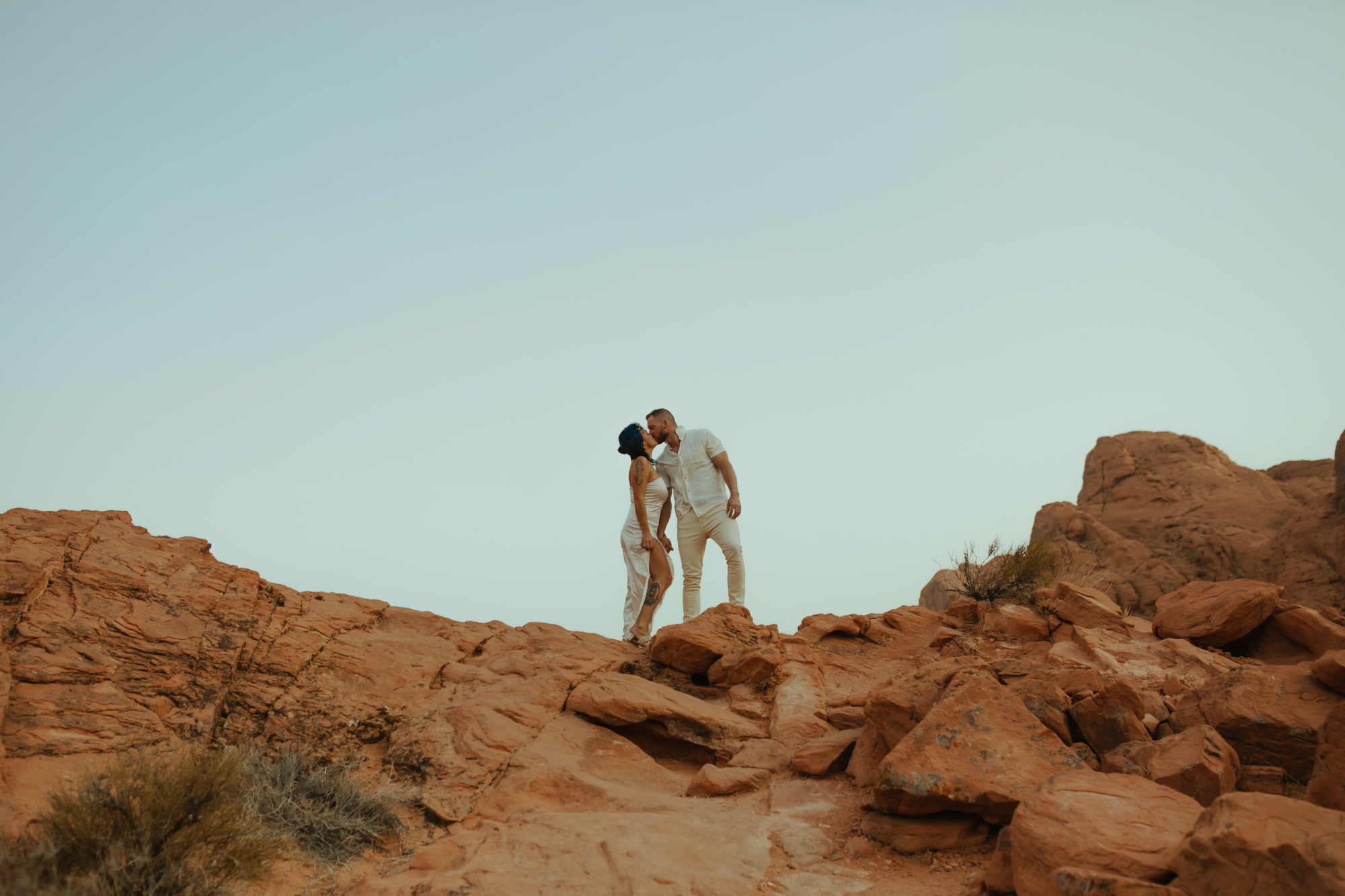 fiance kissing his fiancee as they stand on a cliff edge in valley of fire during a dust storm