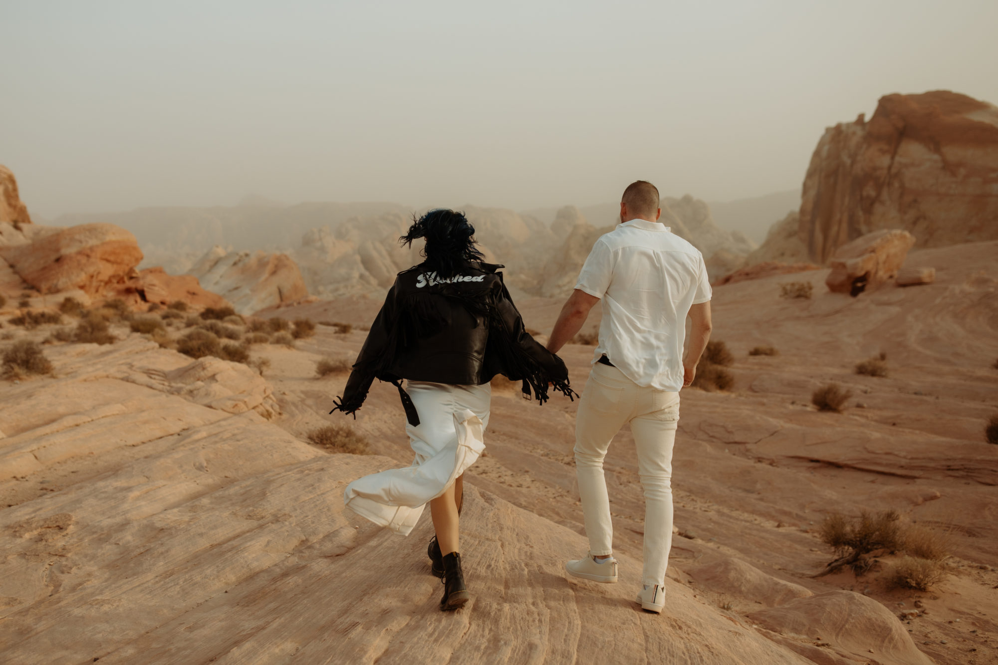 couple holding hands walking away from the camera on the white rocks in valley of fire during a dust storm