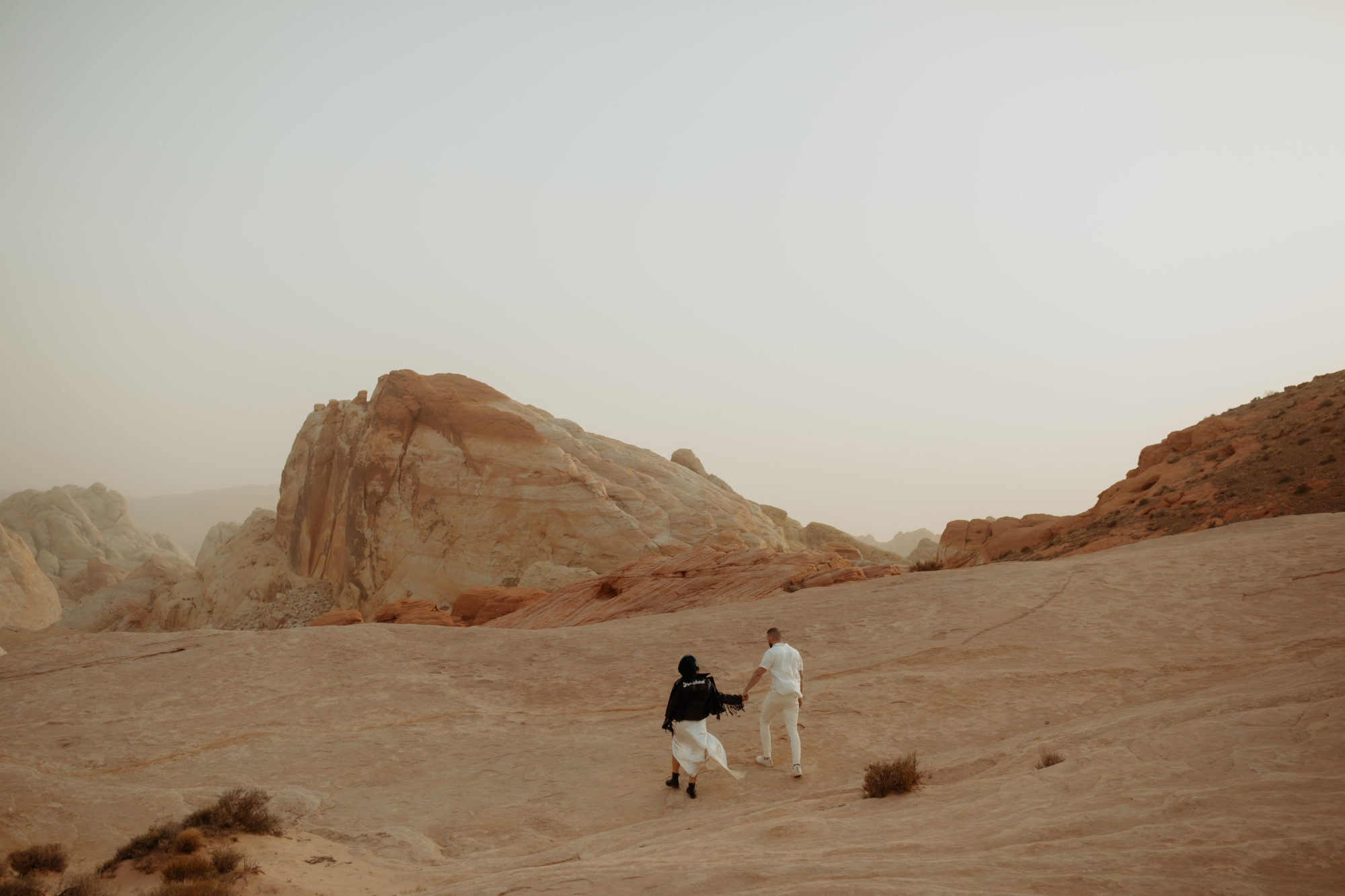 engaged couple holding hands walking through the white rocks of valley of fire during a dust storm
