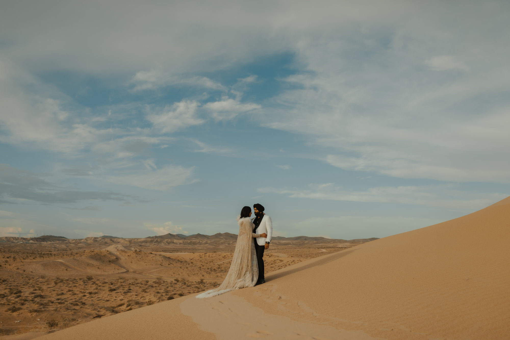 bride and groom standing on a sand dune hugging in the nevada desert