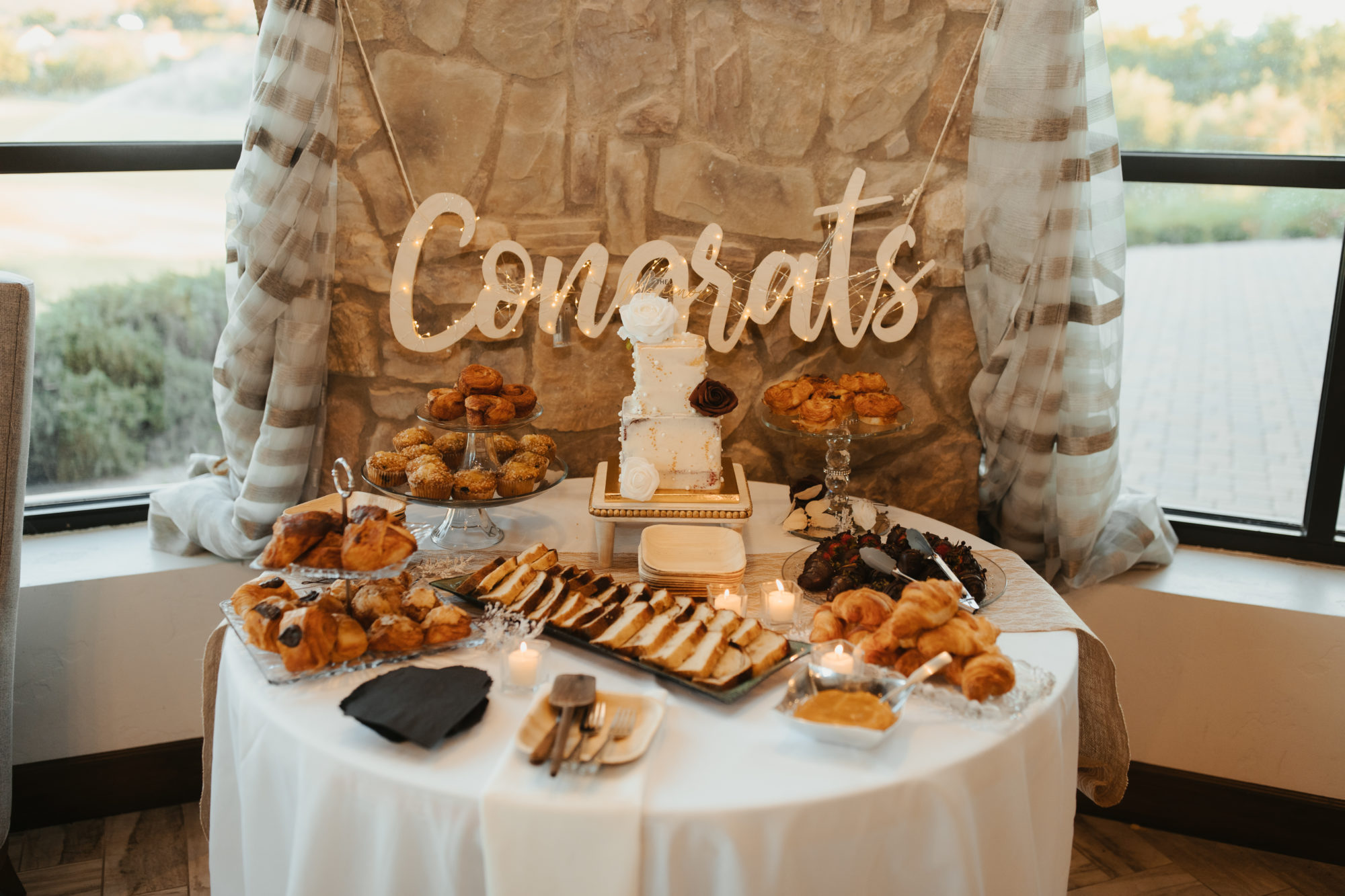 wedding cake pictured on a table with other snacks surrounding it. 