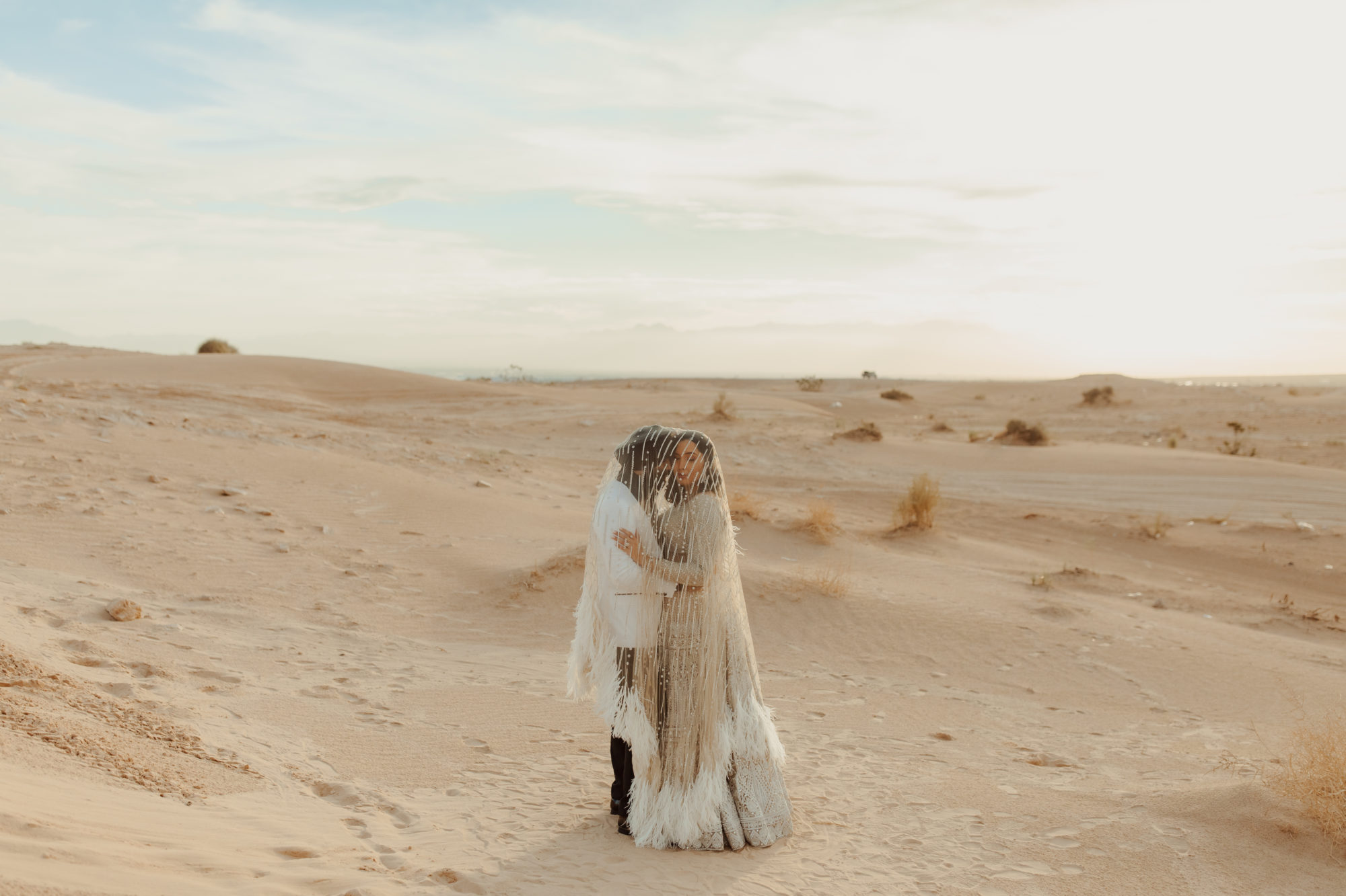 bride and groom standing under her veil in the Nevada desert sand dunes