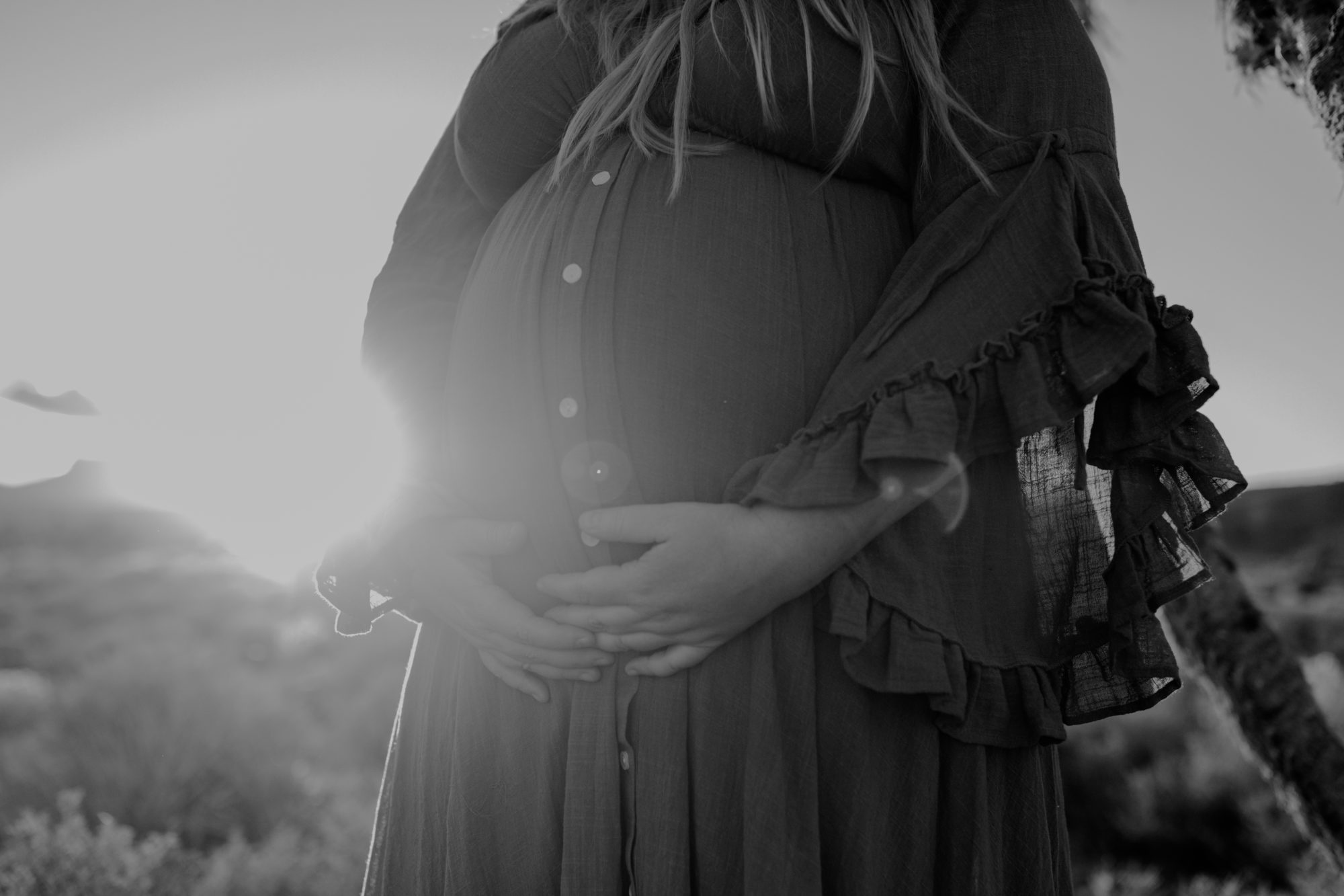 Woman holding pregnant belly during desert sunset photos