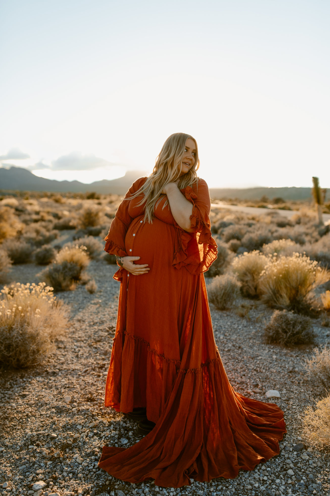 Woman holding pregnant belly during desert photoshoot 